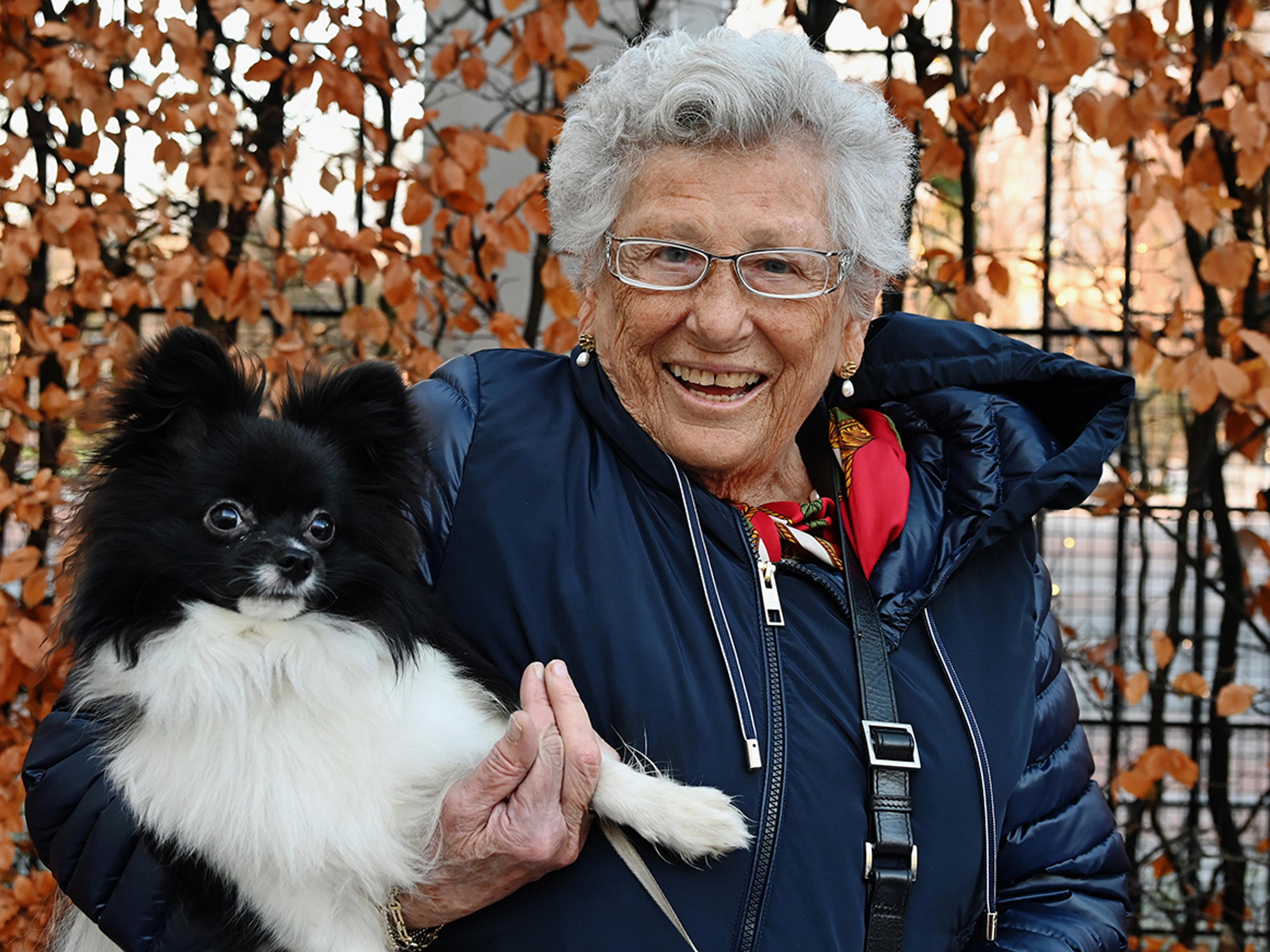 En smilende Prinsesse Astrid med vinterjakke og høstløv i bakgrunnen. Hun har sort-hvite Tarzan på armen.