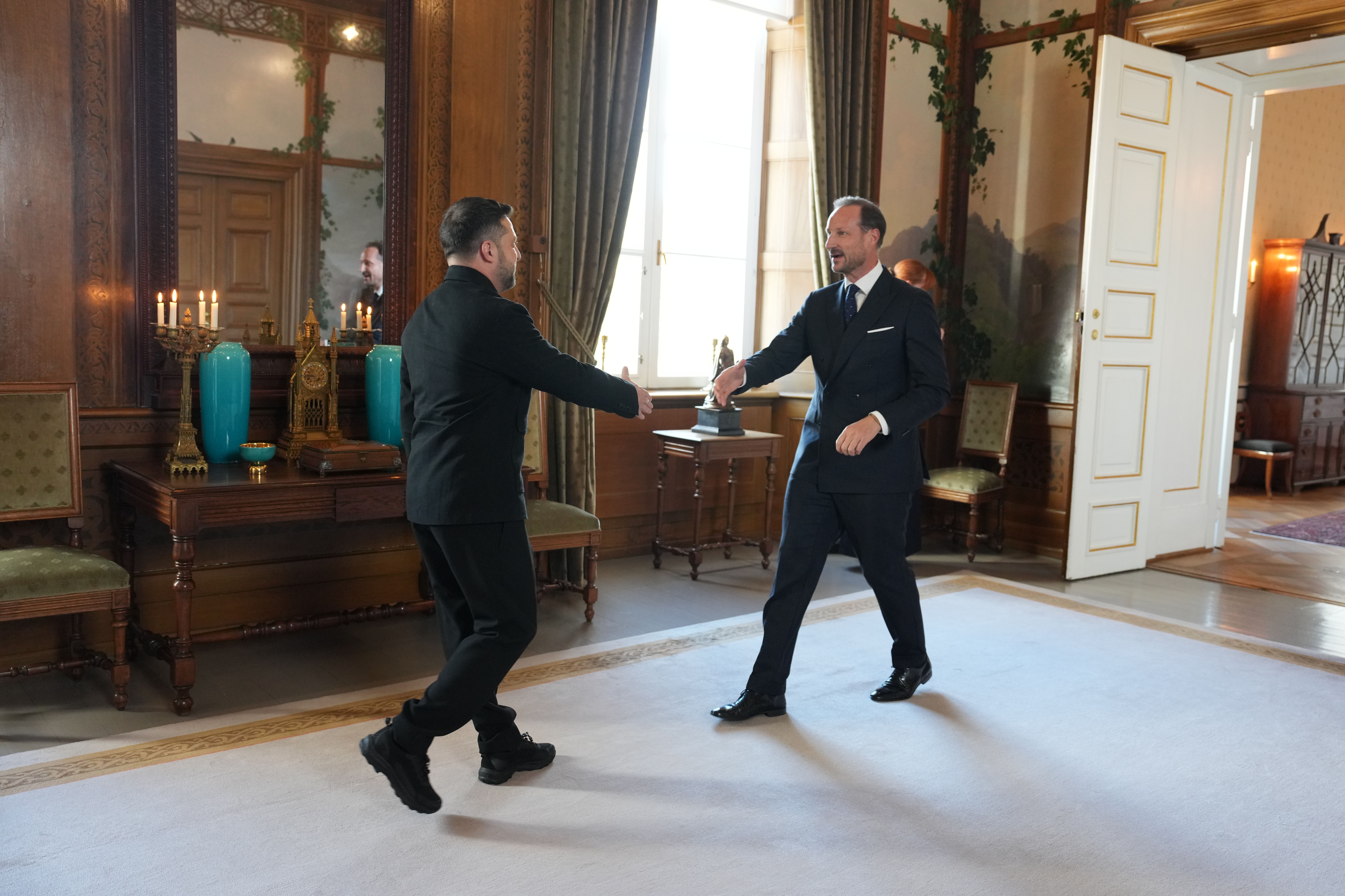 Kongen og presidenten går mot hverandre med utstrakt hånd for å hilse. De er i Fugleværelset, og døren til Kongens kontor står åpen bak Kong Haakon.