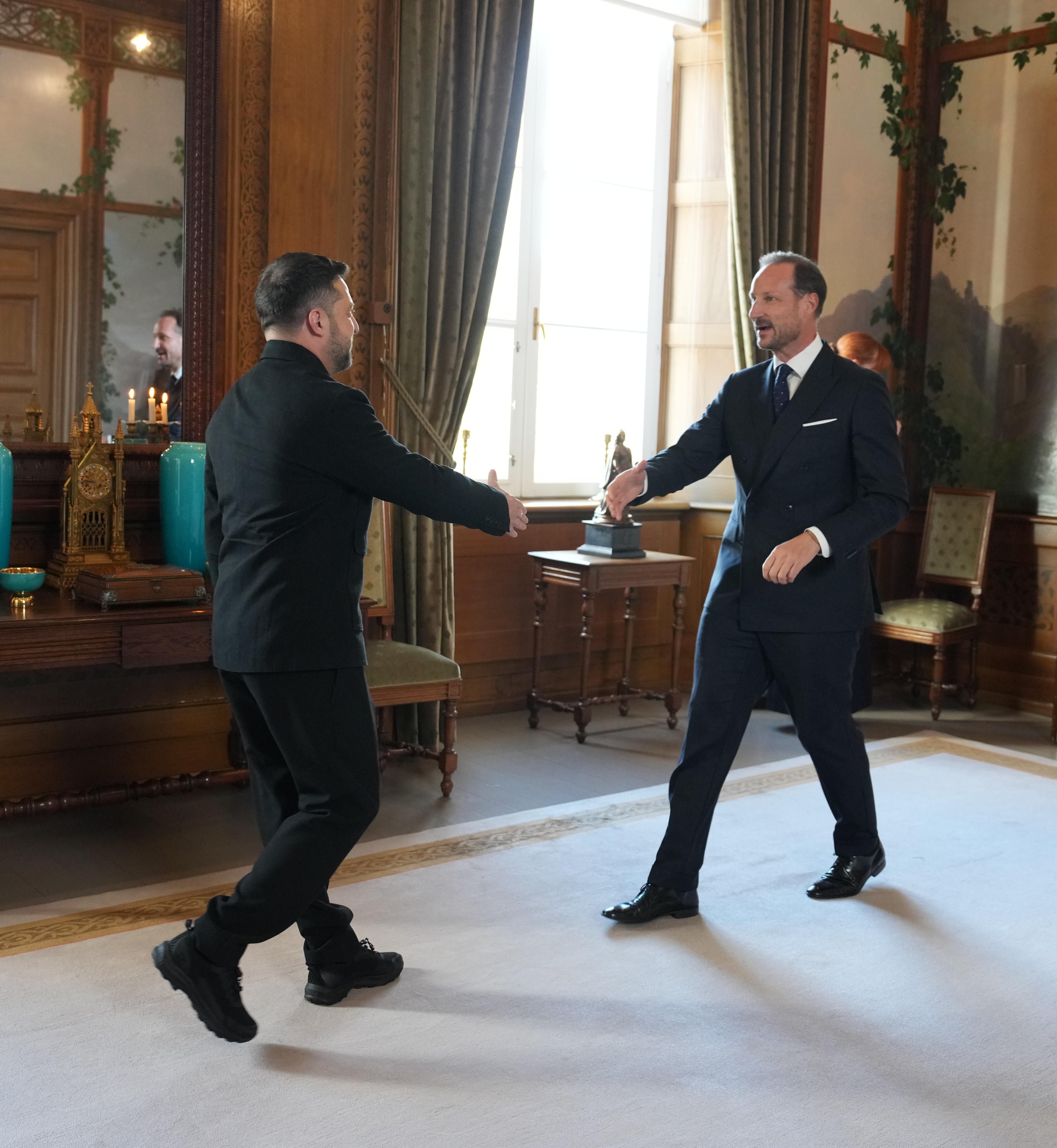 Kongen og presidenten går mot hverandre med utstrakt hånd for å hilse. De er i Fugleværelset, og døren til Kongens kontor står åpen bak Kong Haakon.