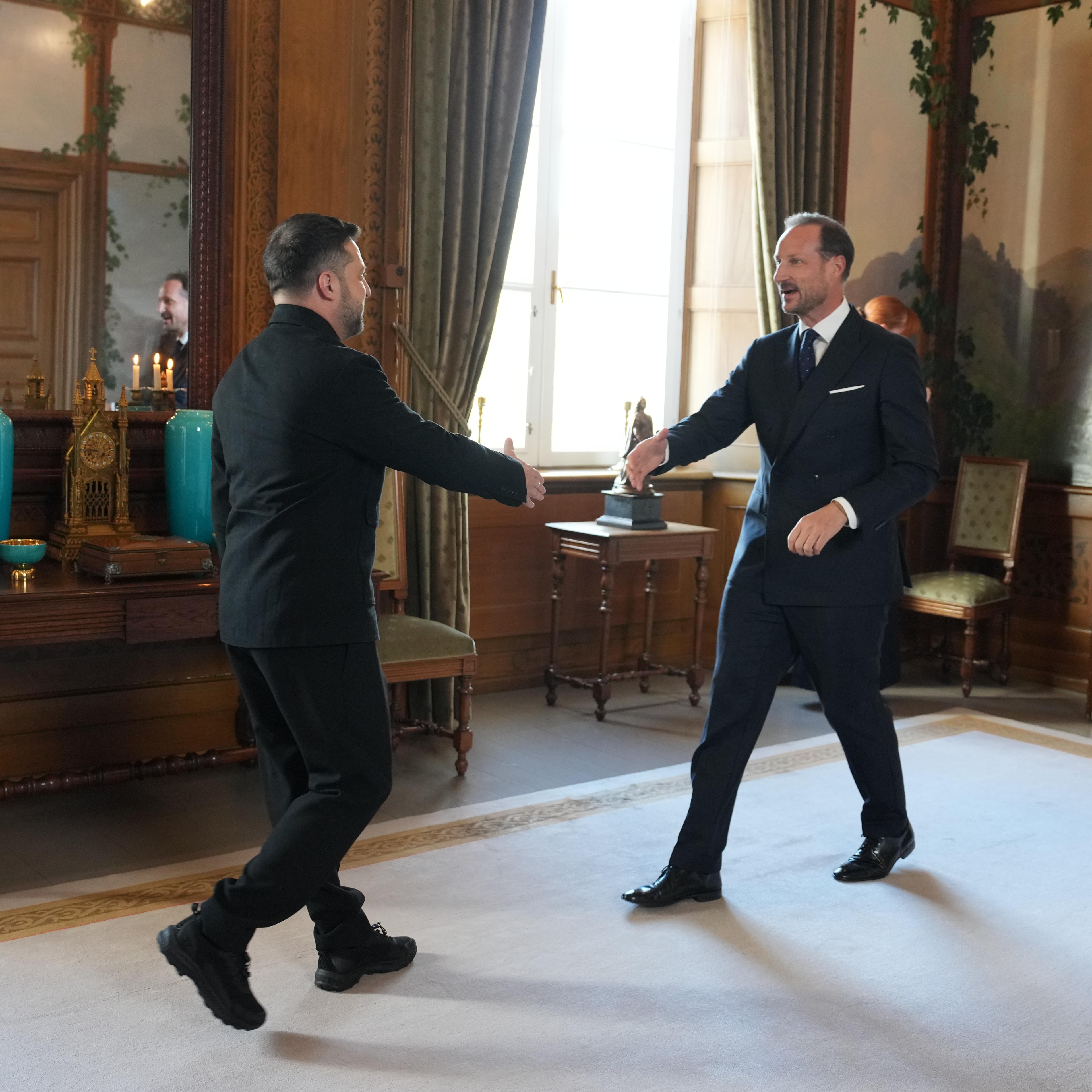 Kongen og presidenten går mot hverandre med utstrakt hånd for å hilse. De er i Fugleværelset, og døren til Kongens kontor står åpen bak Kong Haakon.