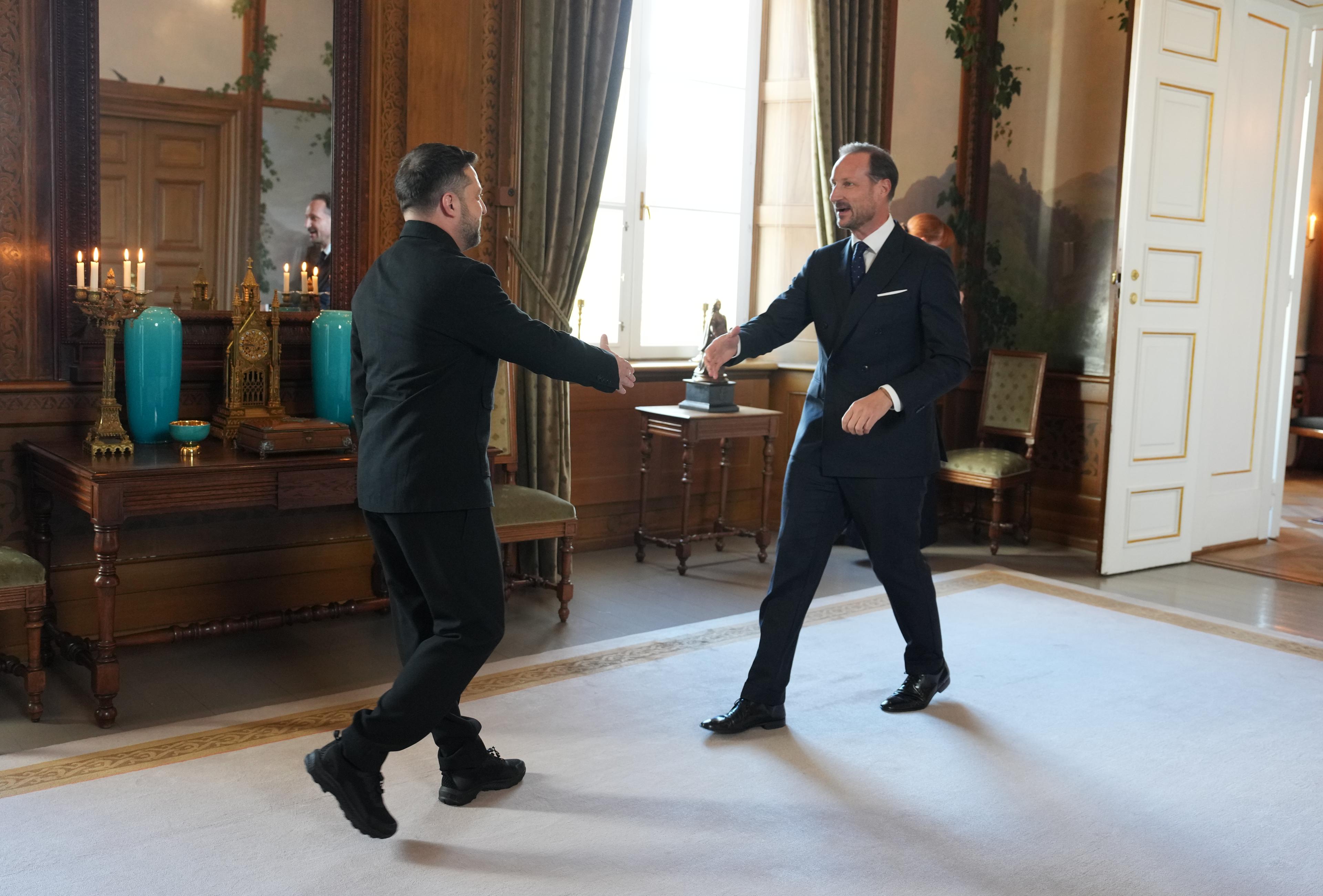 Kongen og presidenten går mot hverandre med utstrakt hånd for å hilse. De er i Fugleværelset, og døren til Kongens kontor står åpen bak Kong Haakon.