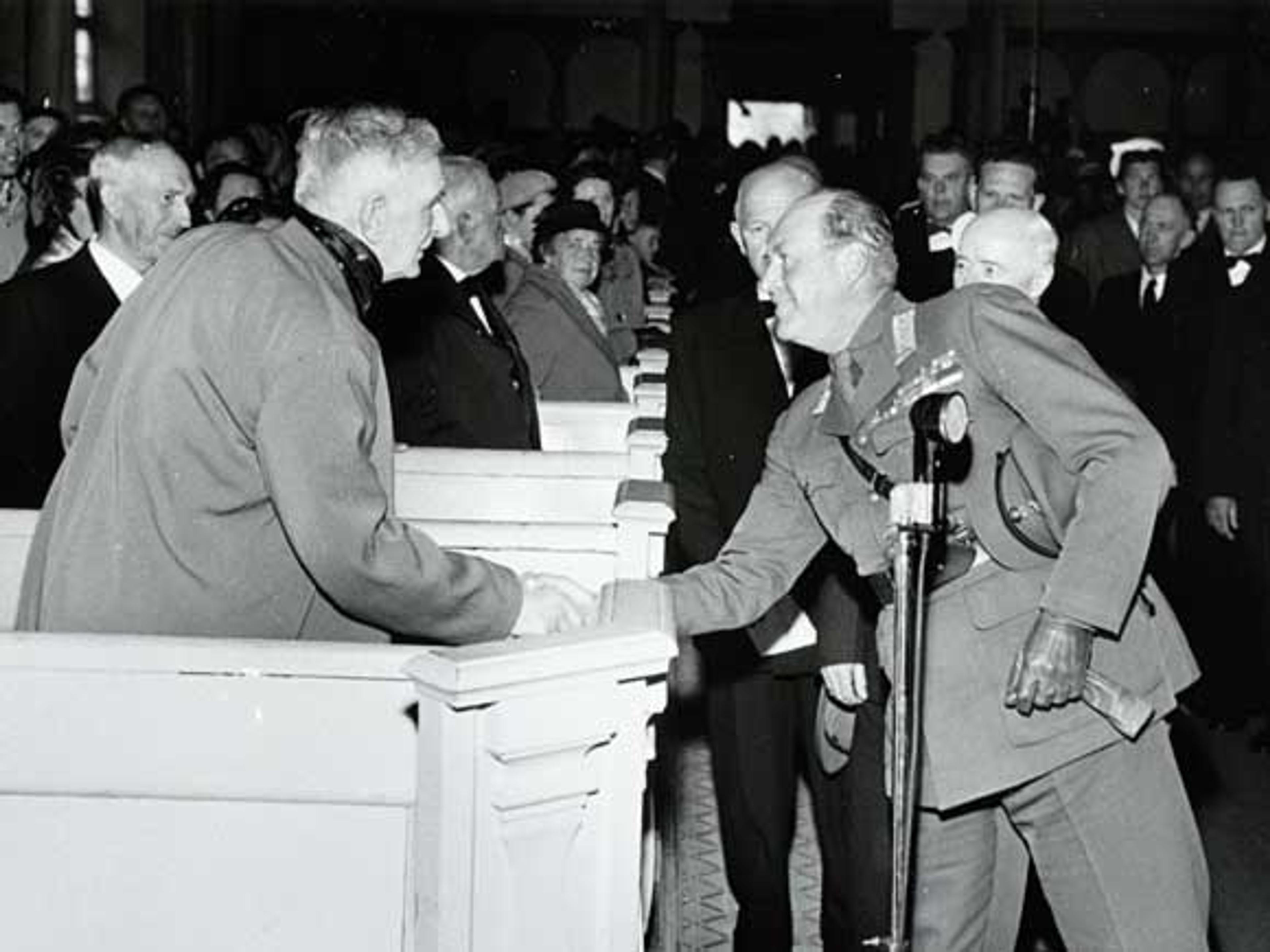 Sort-hvittbilde av Kongen på vei ned midtgangen - har stanset opp og håndhilser på forfatteren, som har reist seg fra kirkebenken,