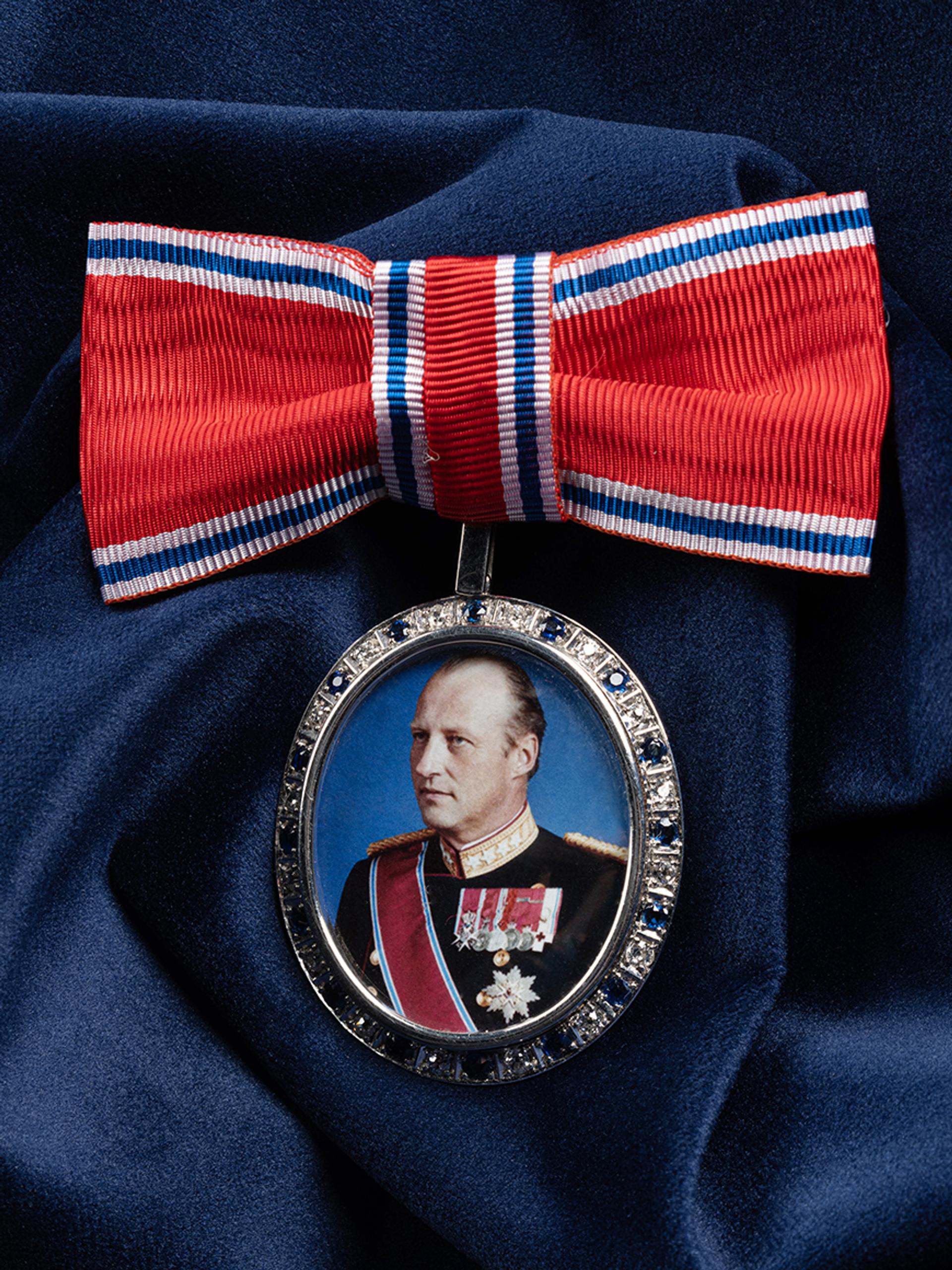 Et portrett av Kong Harald i sløyfe presentert på et blått klede.