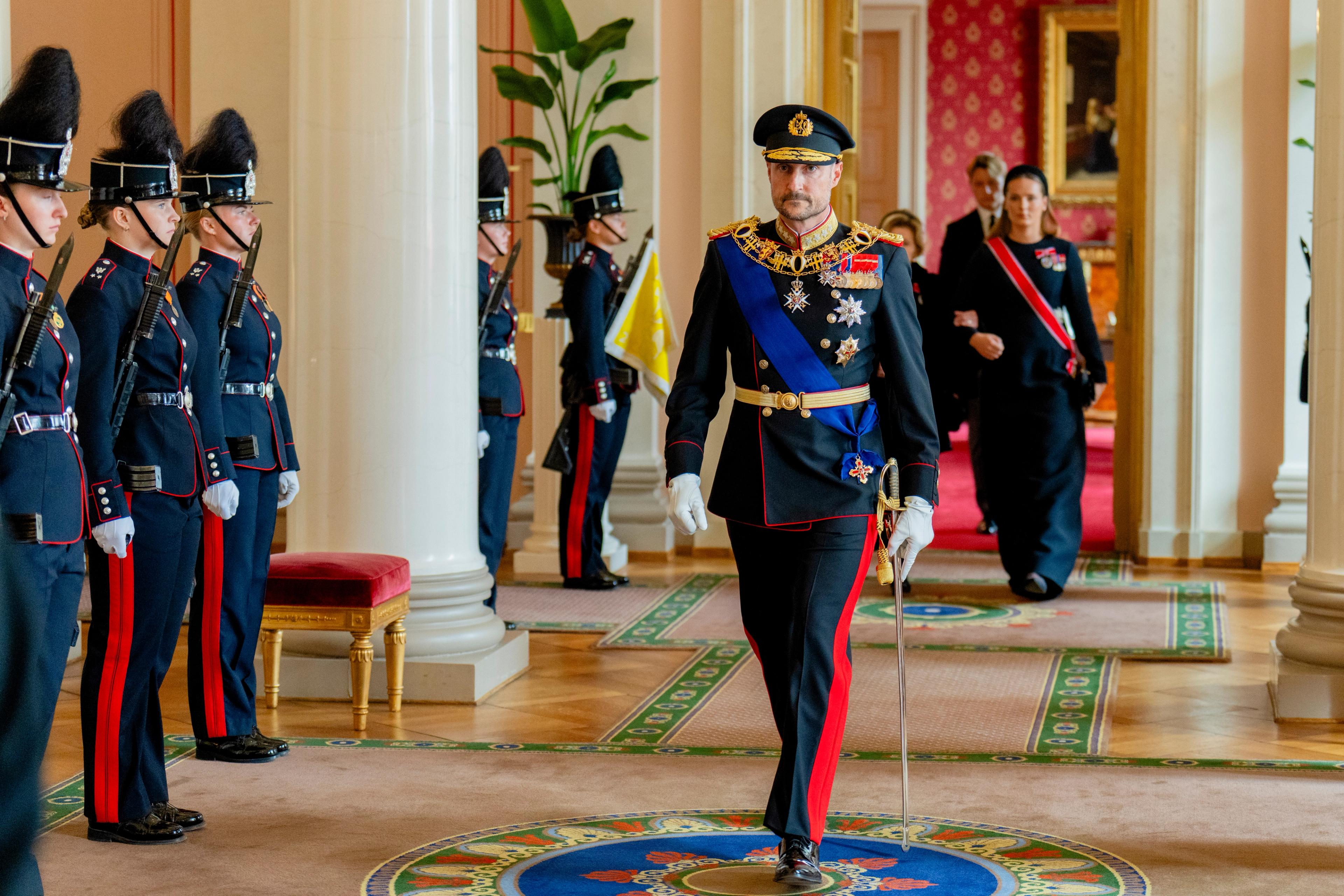Kong Haakon i gallauniform kommer ut i Øvre vestibyle. Bak ham kommer Kronprinsesse Ingrid Alexandra og Dronning Sonja.