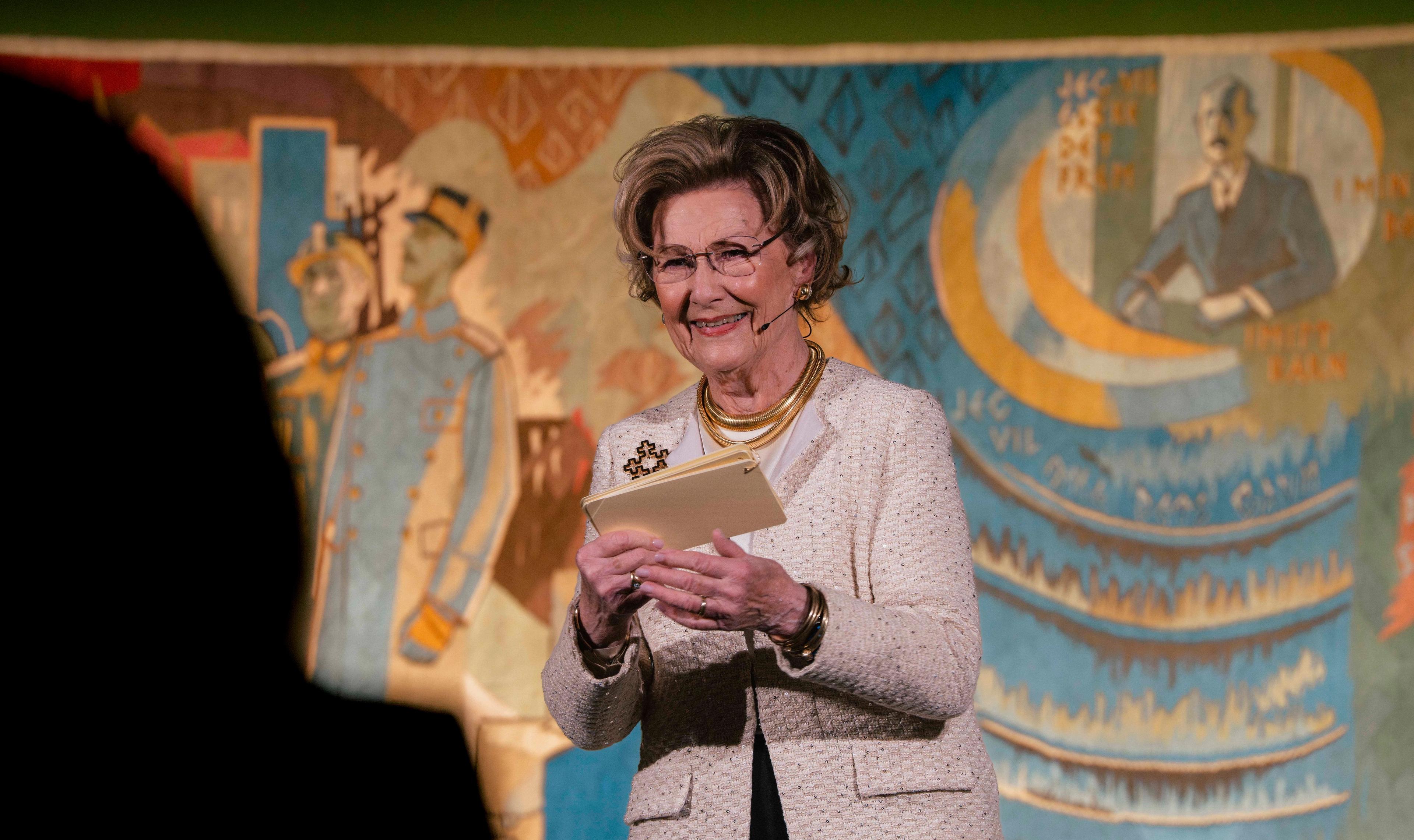 Dronning Sonja på scenen med Kongeteppet i bakgrunnen.