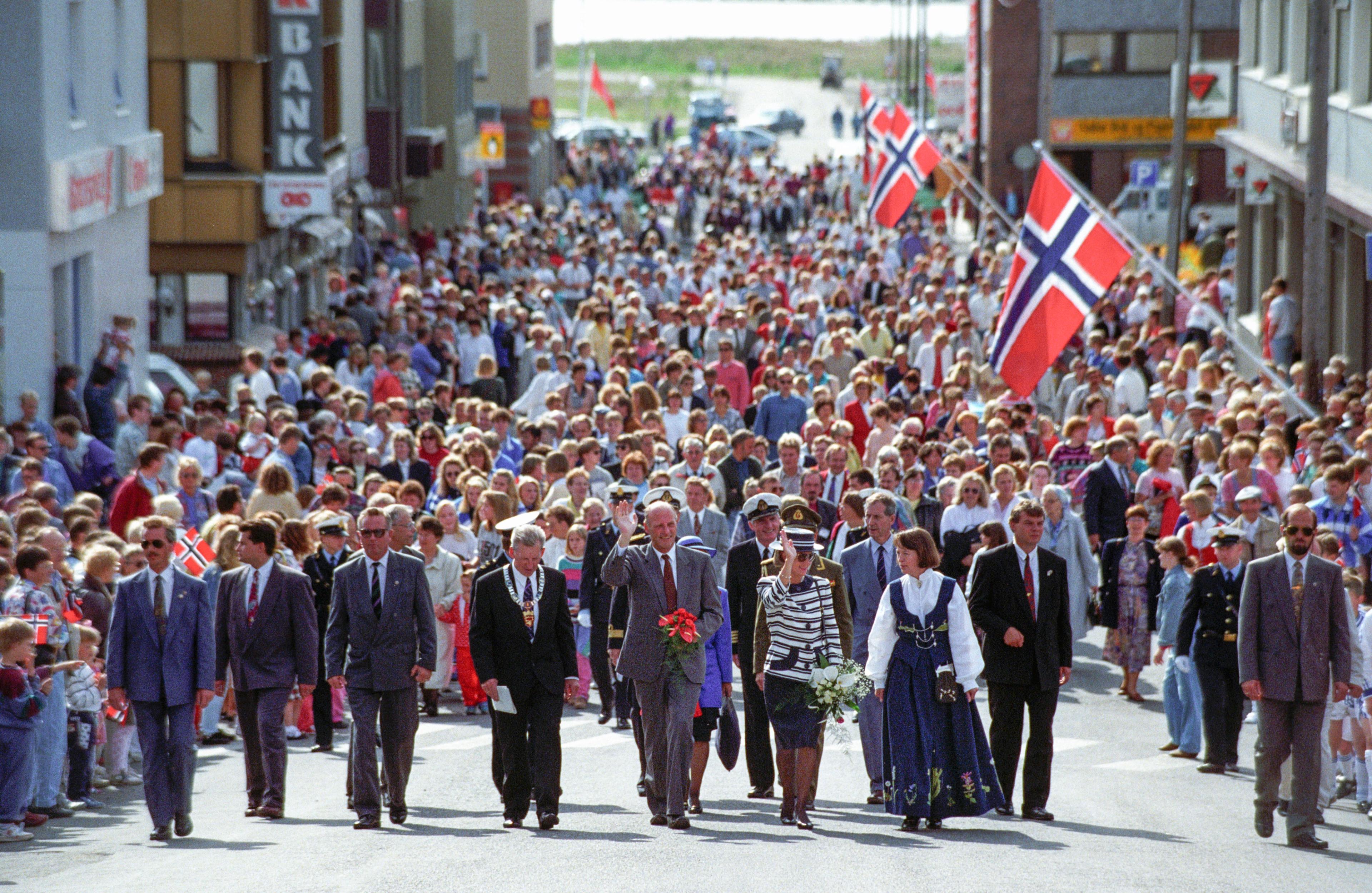 Kongeparet går fremst i en folkemengde og vinker
