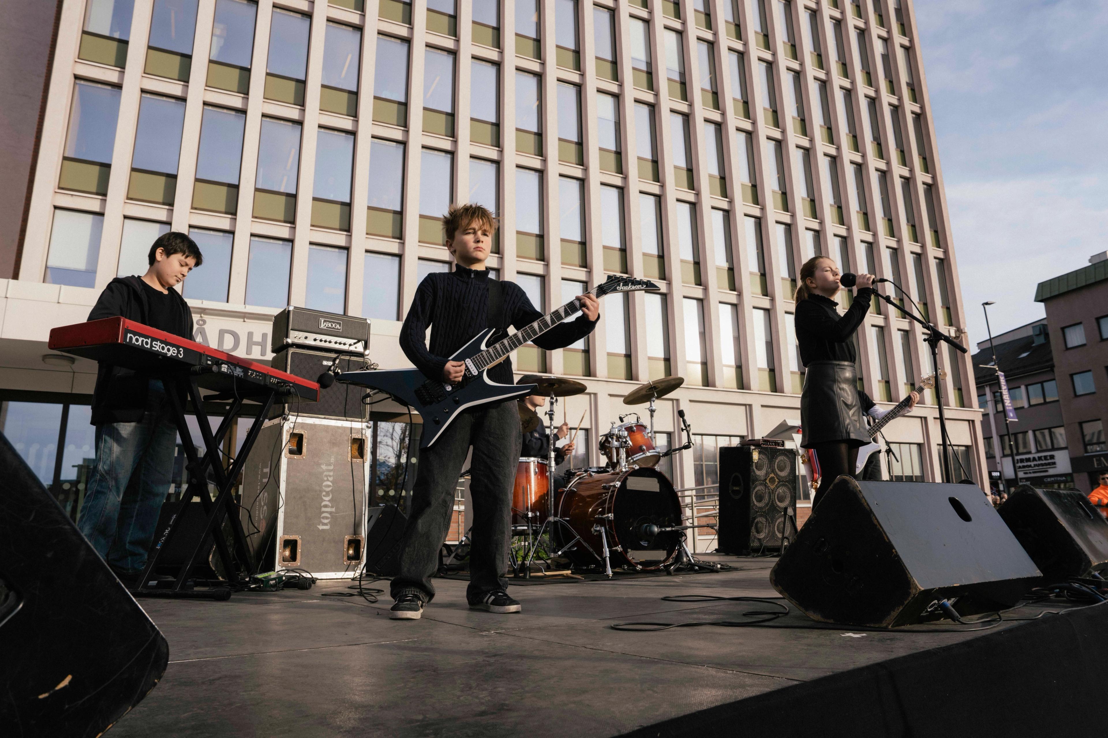Bandet står på scenen. Fremst står gitaristen, med keyboardist og vokalist på hver sin side