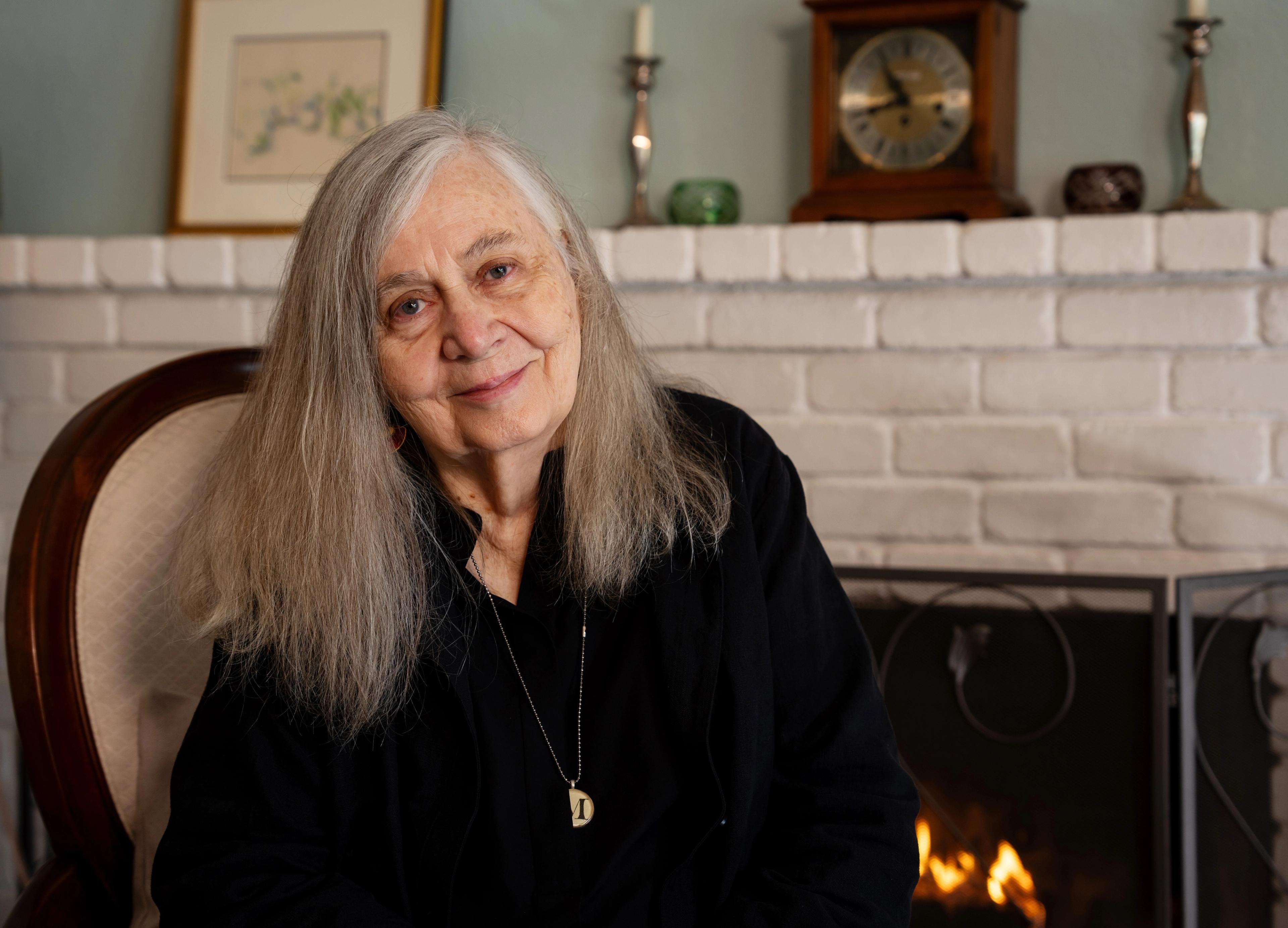 Marilynne Robinson sit smilande framfor ein peis.