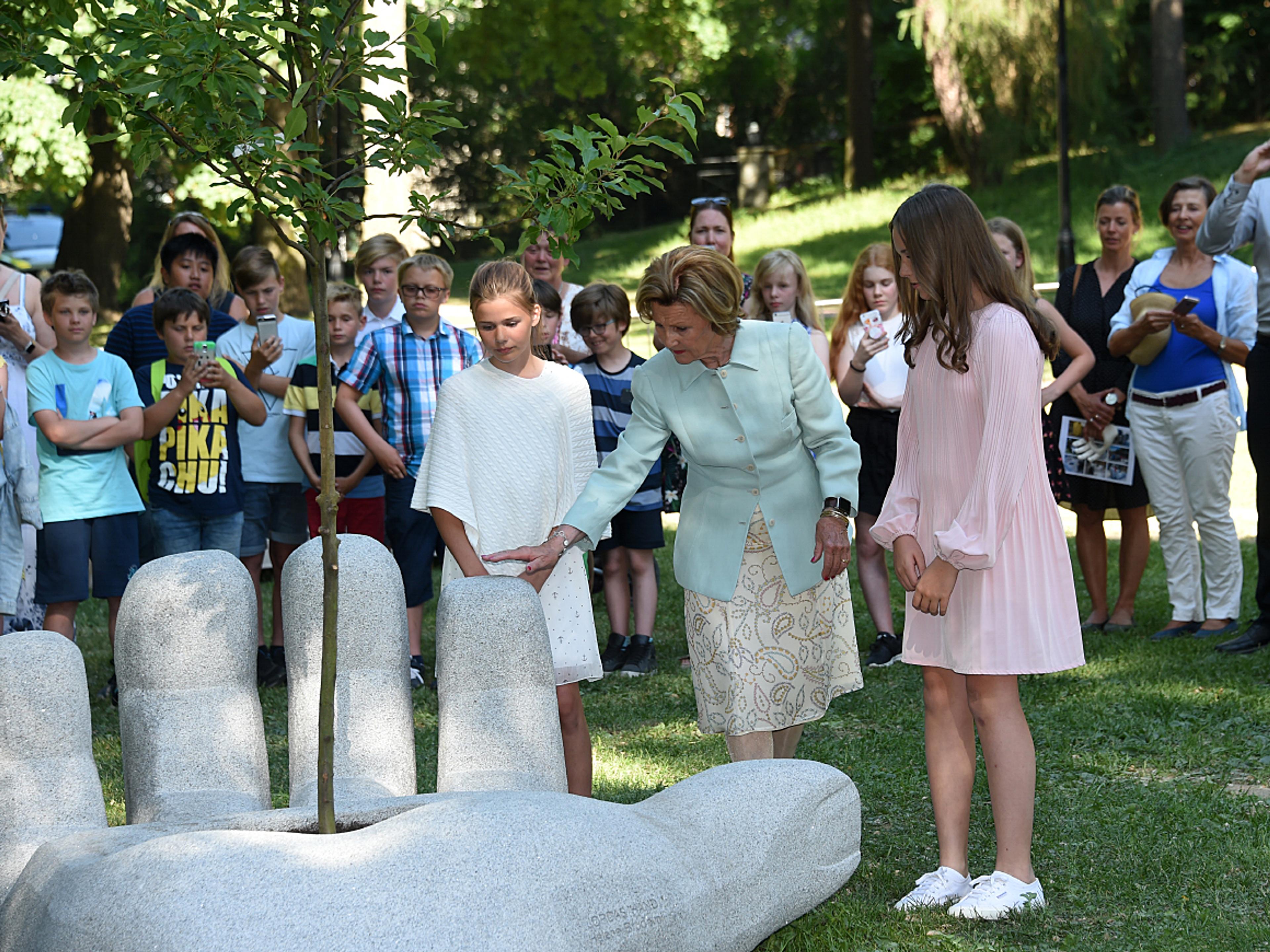 Dronning Sonja og Prinsessen står sammen med skaperen av Jordas hånd: En stor hånd i betong ligger på gresset med håndflaten opp. Det er et bed i midten, og opp fra dette vokser det et tre.