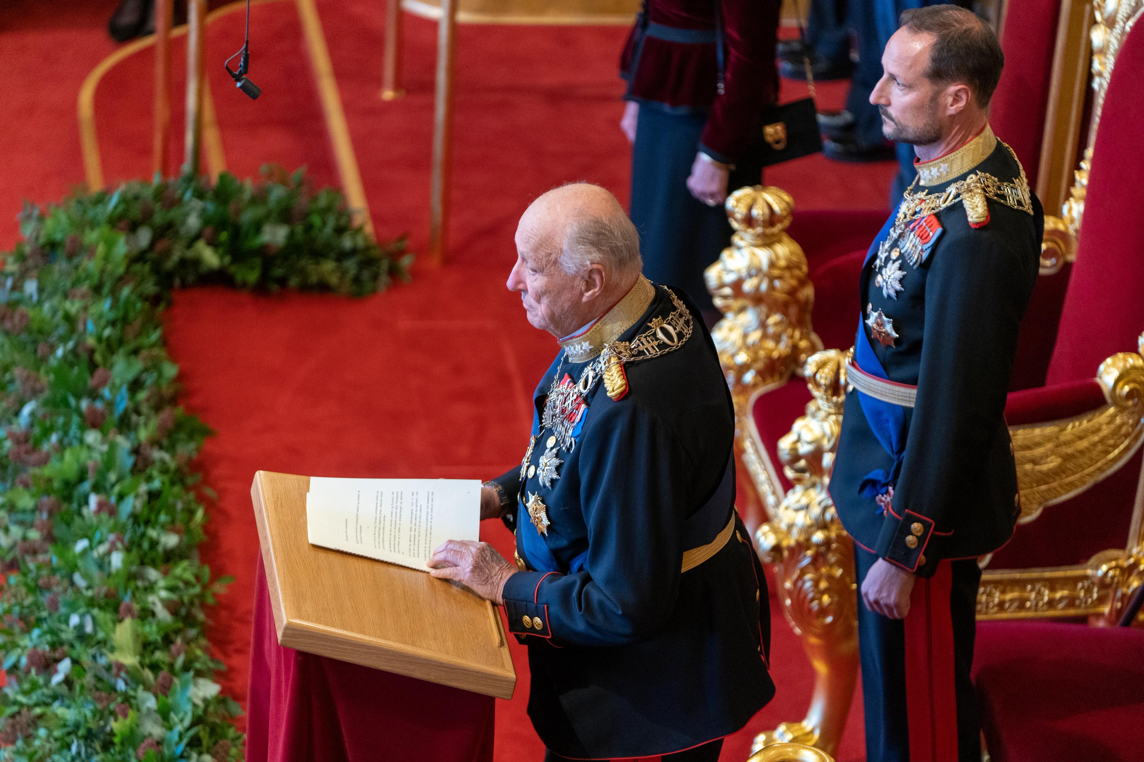 Kong Harald står på talerstolen i Stortinget. Rett bak står Kronprins Haakon.