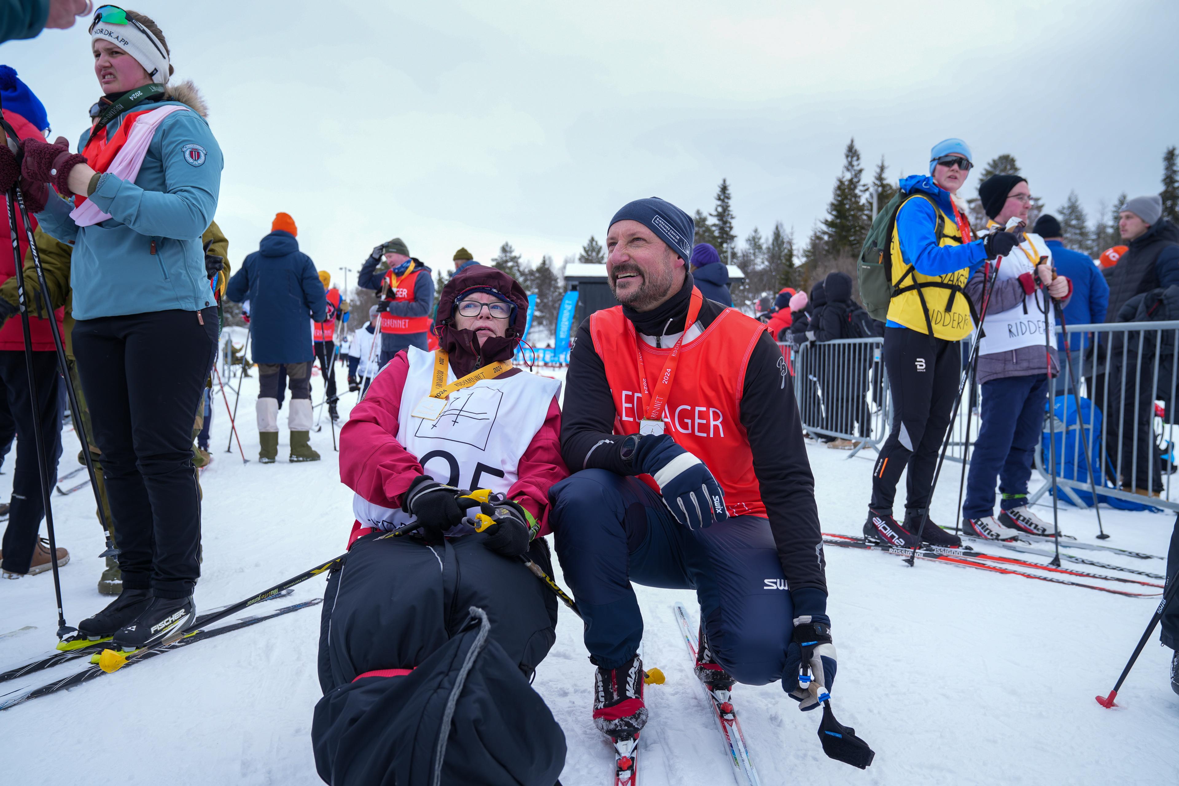 Kronprinsen i sportsutstyr sitter på huk ved siden av en parautøver i kjelke.