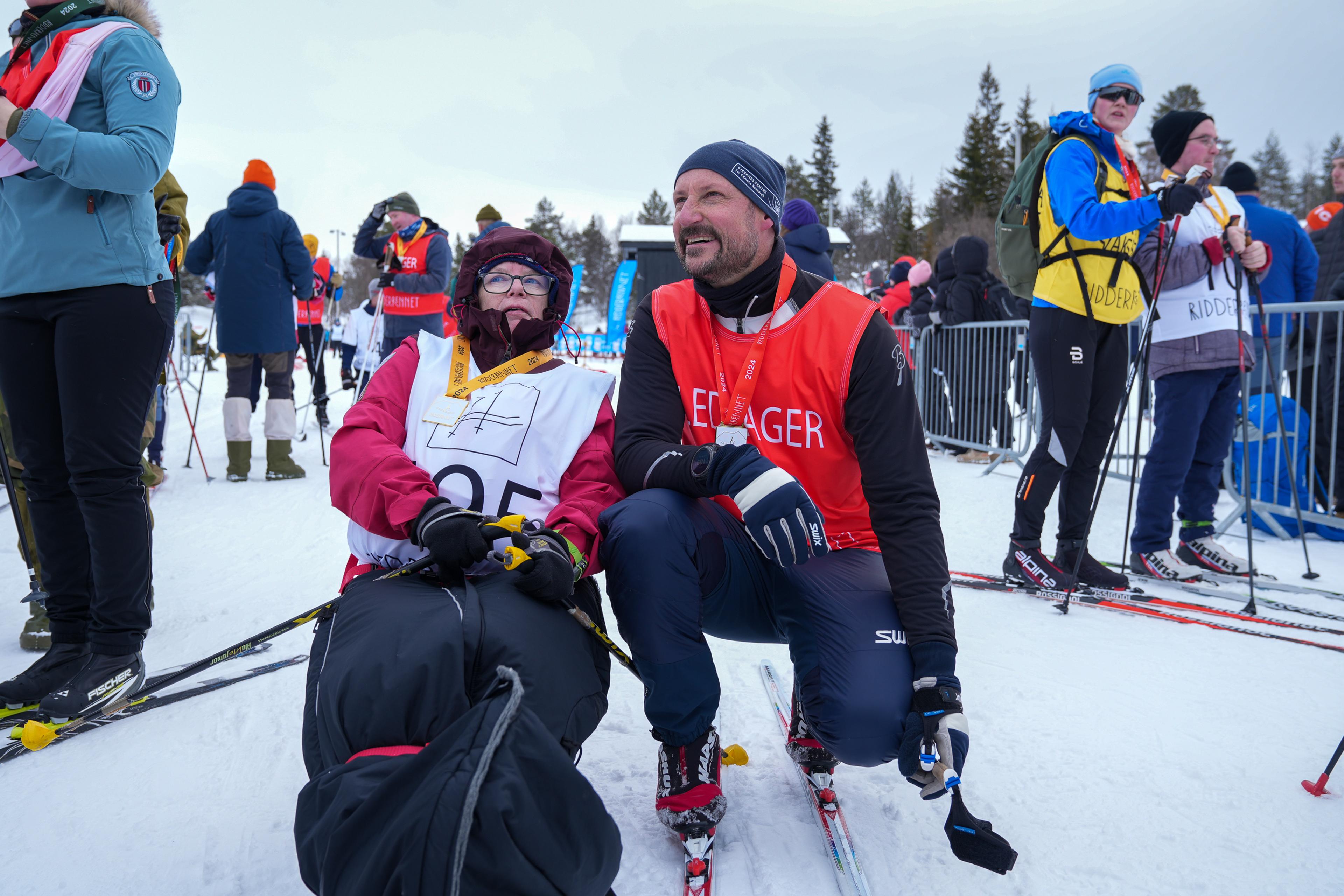 Kronprinsen i sportsutstyr sitter på huk ved siden av en parautøver i kjelke.