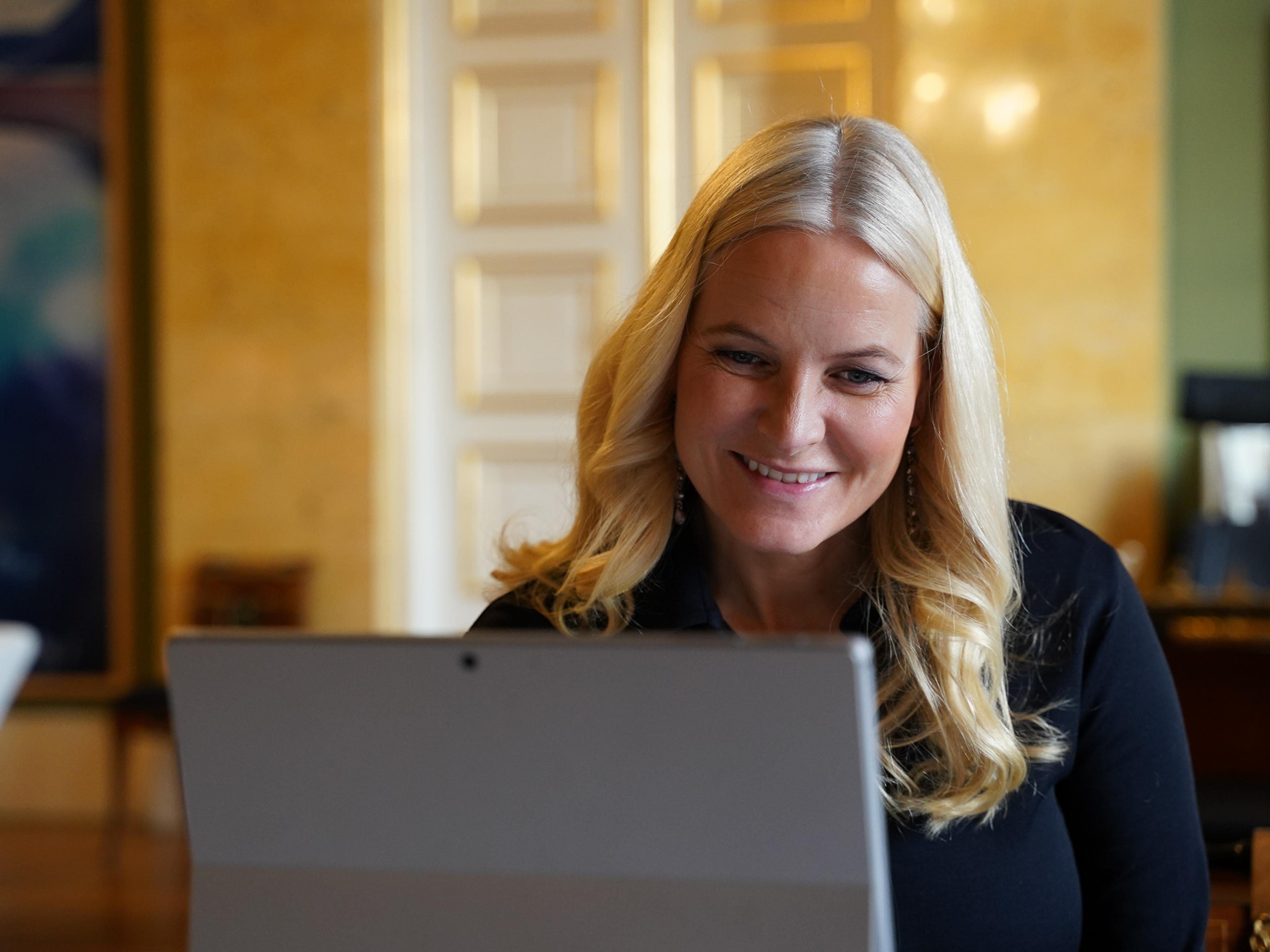 Kronprinsesse Mette-Marit ser smilende inn i skjermen på datamaskinen foran henne.