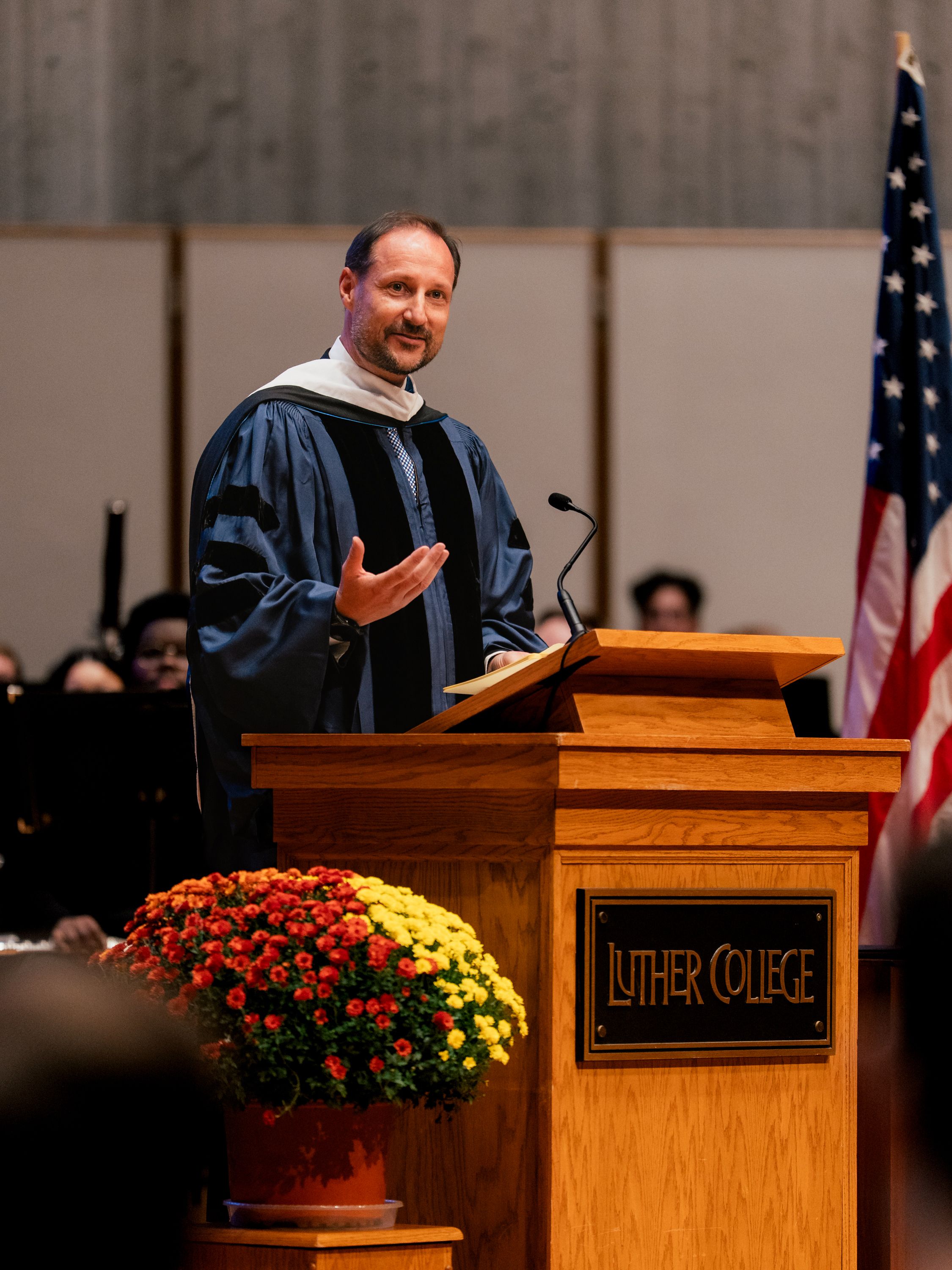 Kronprinsen på talerstolen. Han er kledd i universitetets kappe og et amerikansk flagg står ved siden av.