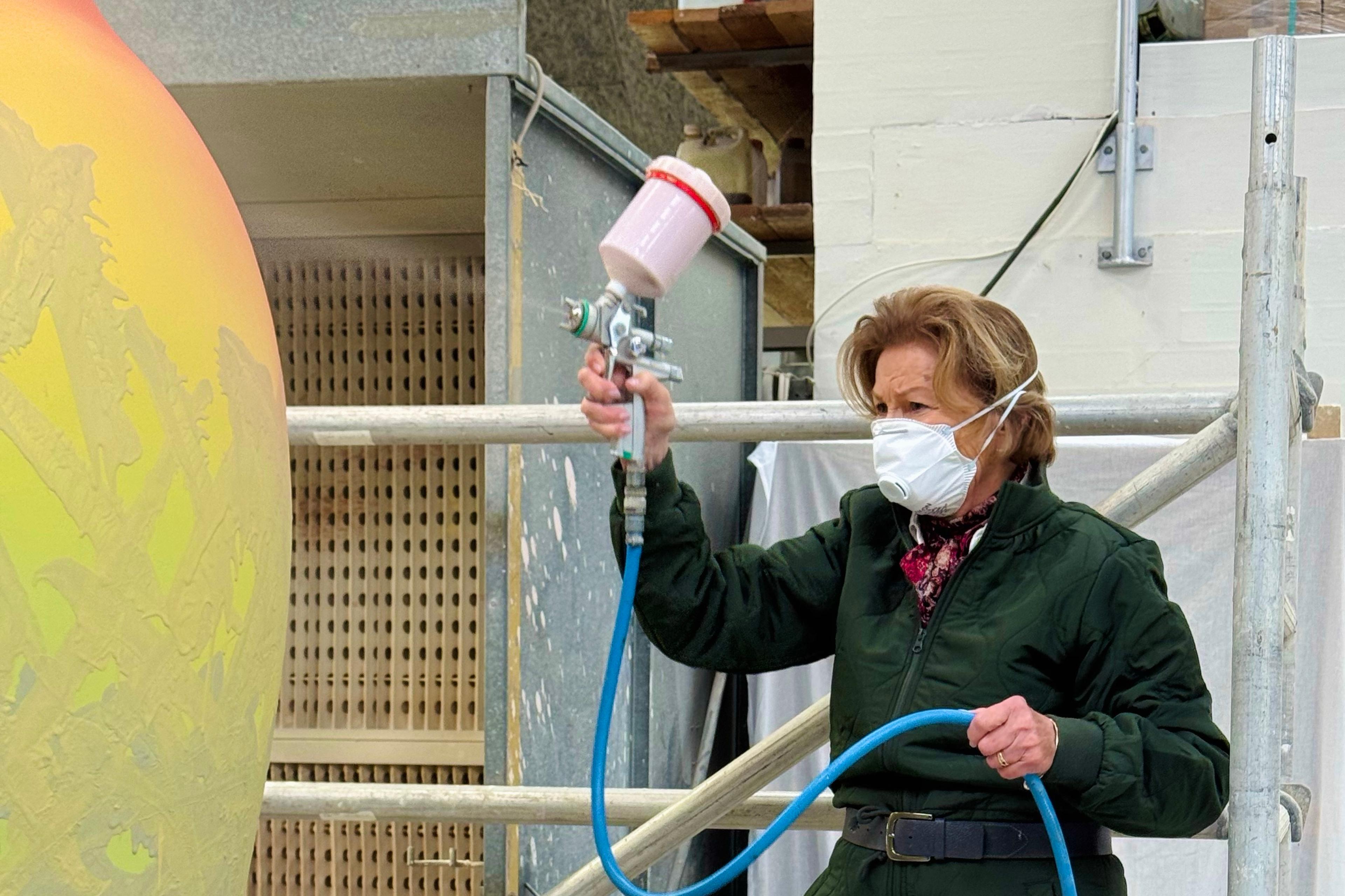 Dronning Sonja i arbeidstøy og munnbind foran den ene krukken.