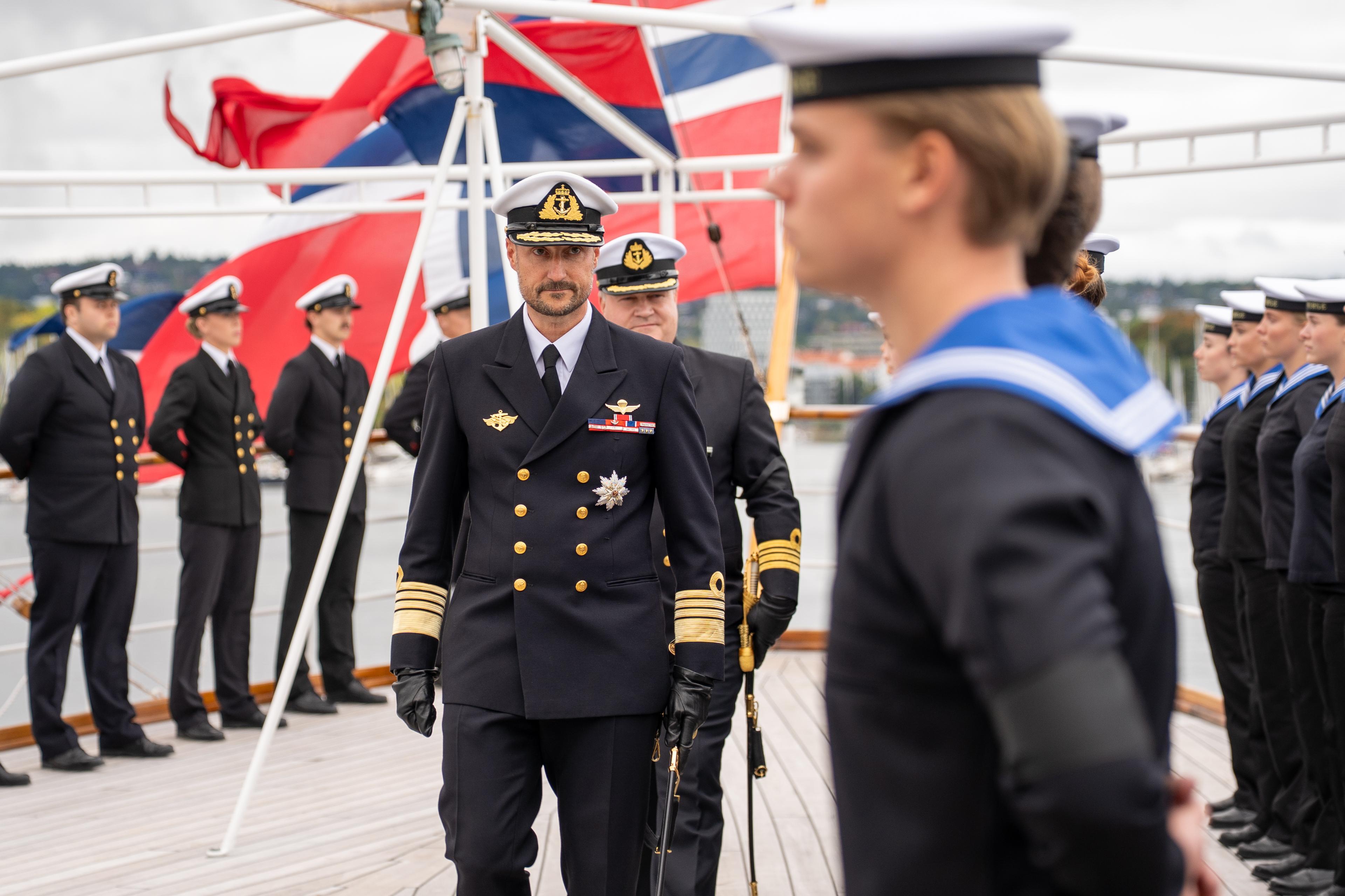 Kong Haakon passerer ei rekkje vernepliktige, medan skipssjefen går bak.