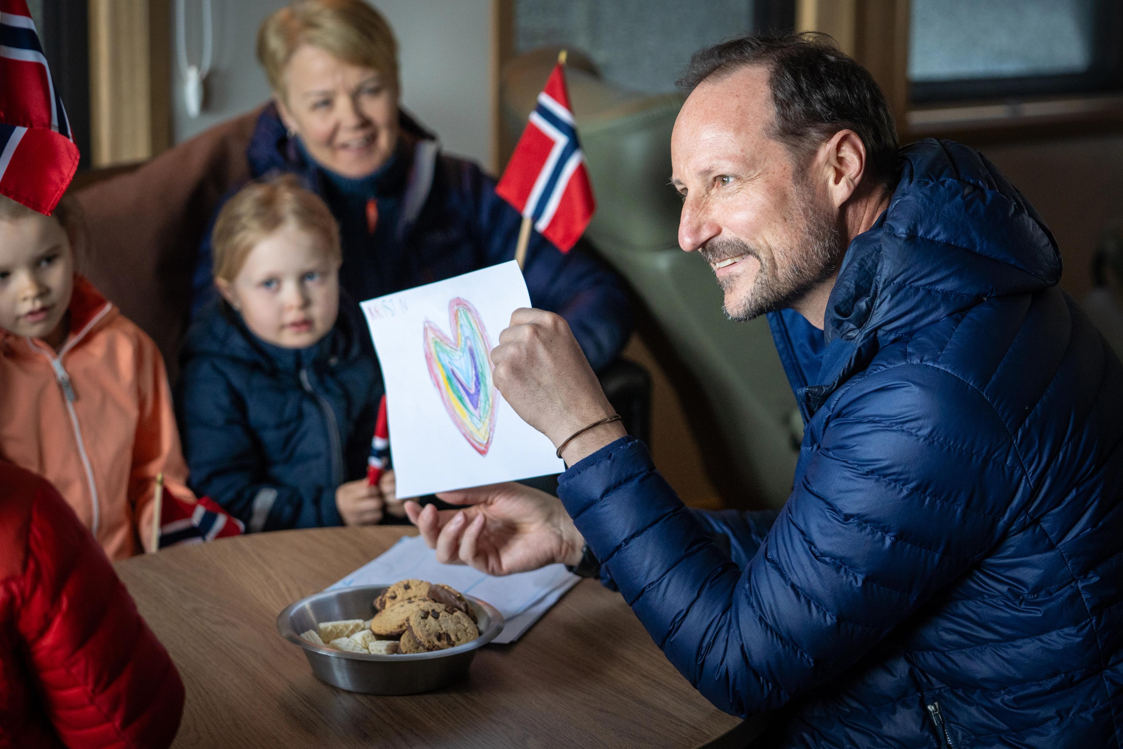 Kronprinsen smiler til barn rundt bordet. Han holder en fargeglad tegning av et hjerte.