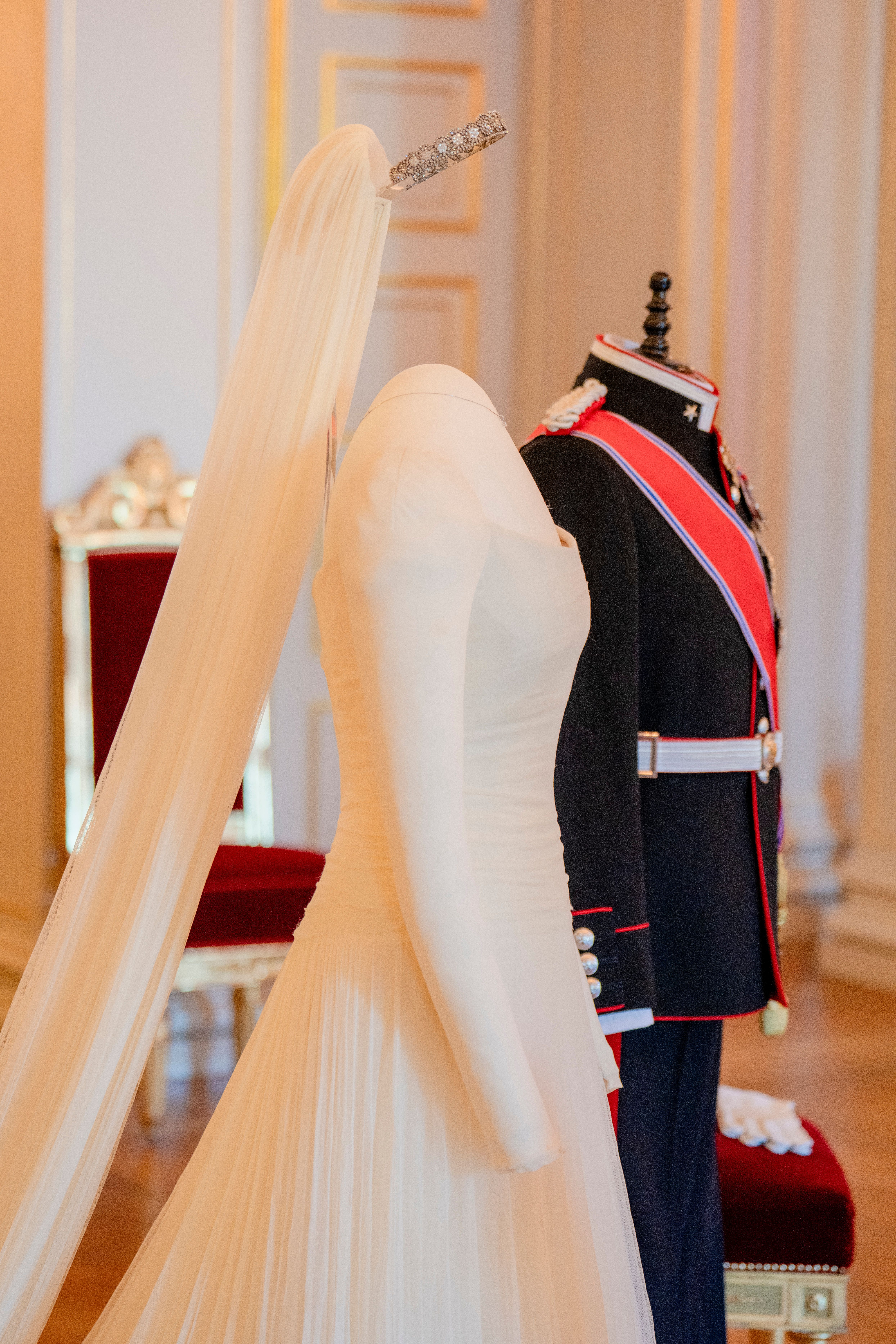 To utstillingdukker står oppstilt med henholdsvis Kronprinsens gallauniform og Kronprinsessens brudekjole med langt slørt og slep.