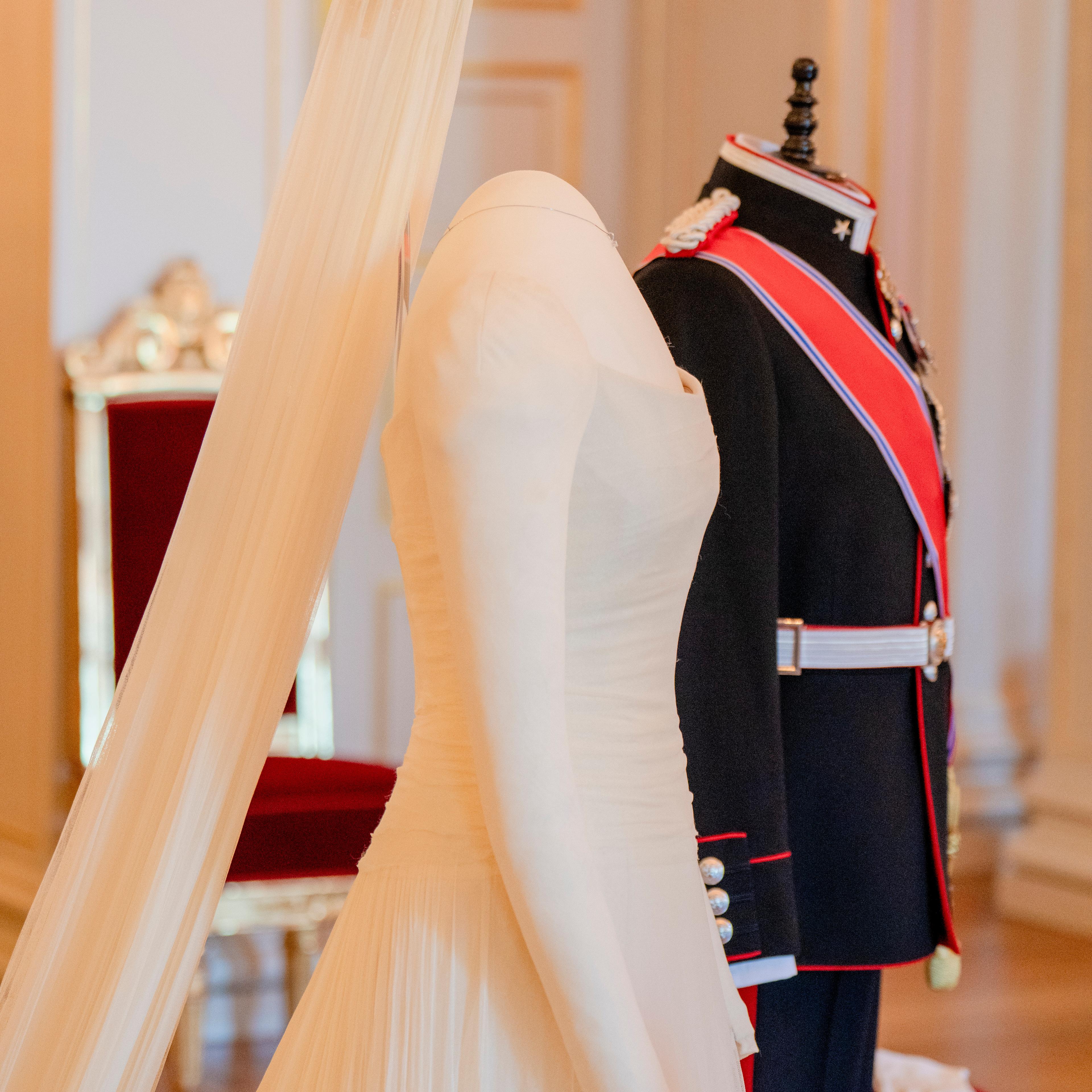 To utstillingdukker står oppstilt med henholdsvis Kronprinsens gallauniform og Kronprinsessens brudekjole med langt slørt og slep.