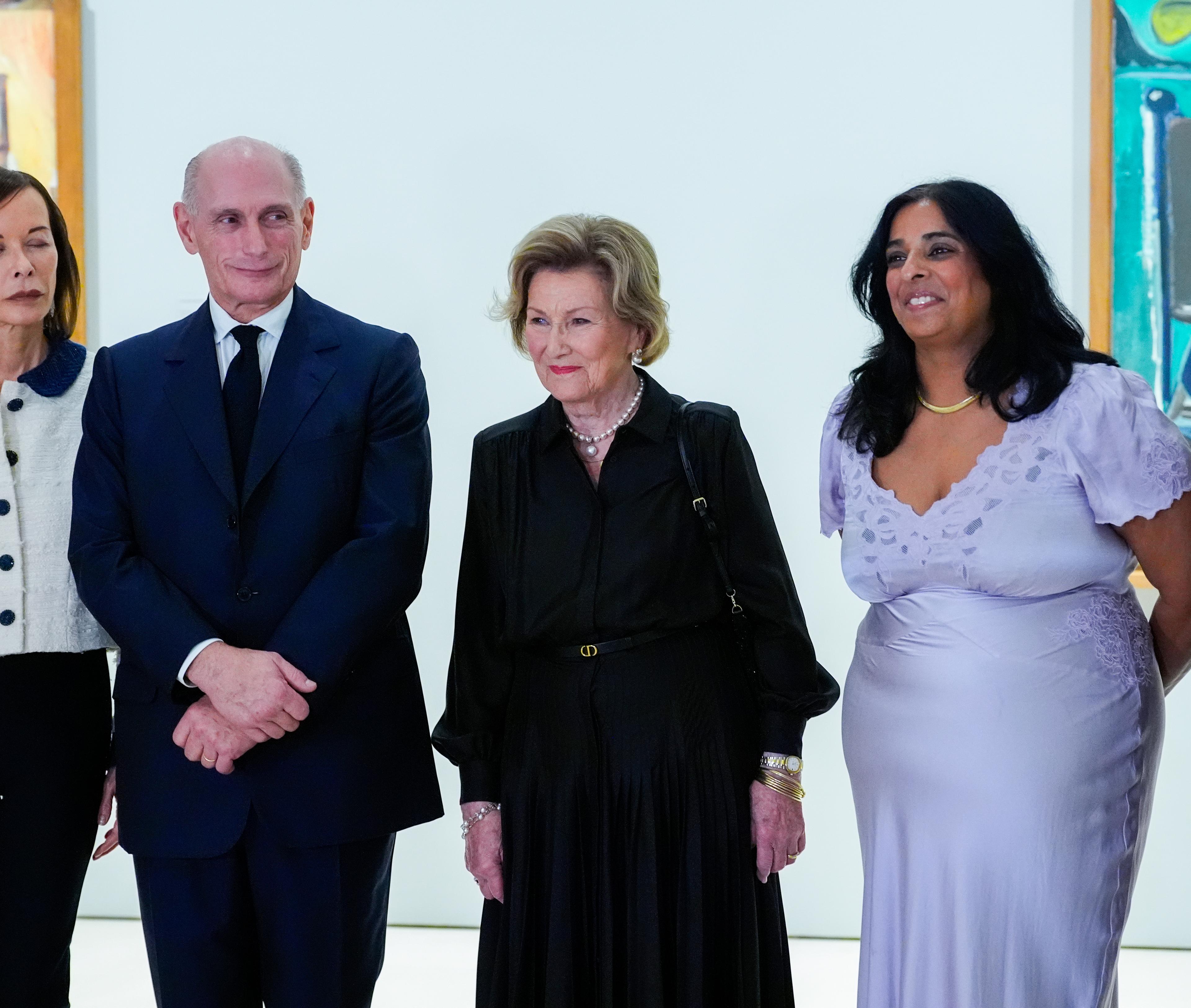 Dronning Sonja i sort står sentralt i bildet, mellom andre deltakere på omvisningen. Malerier skimtes i bakgrunnen.