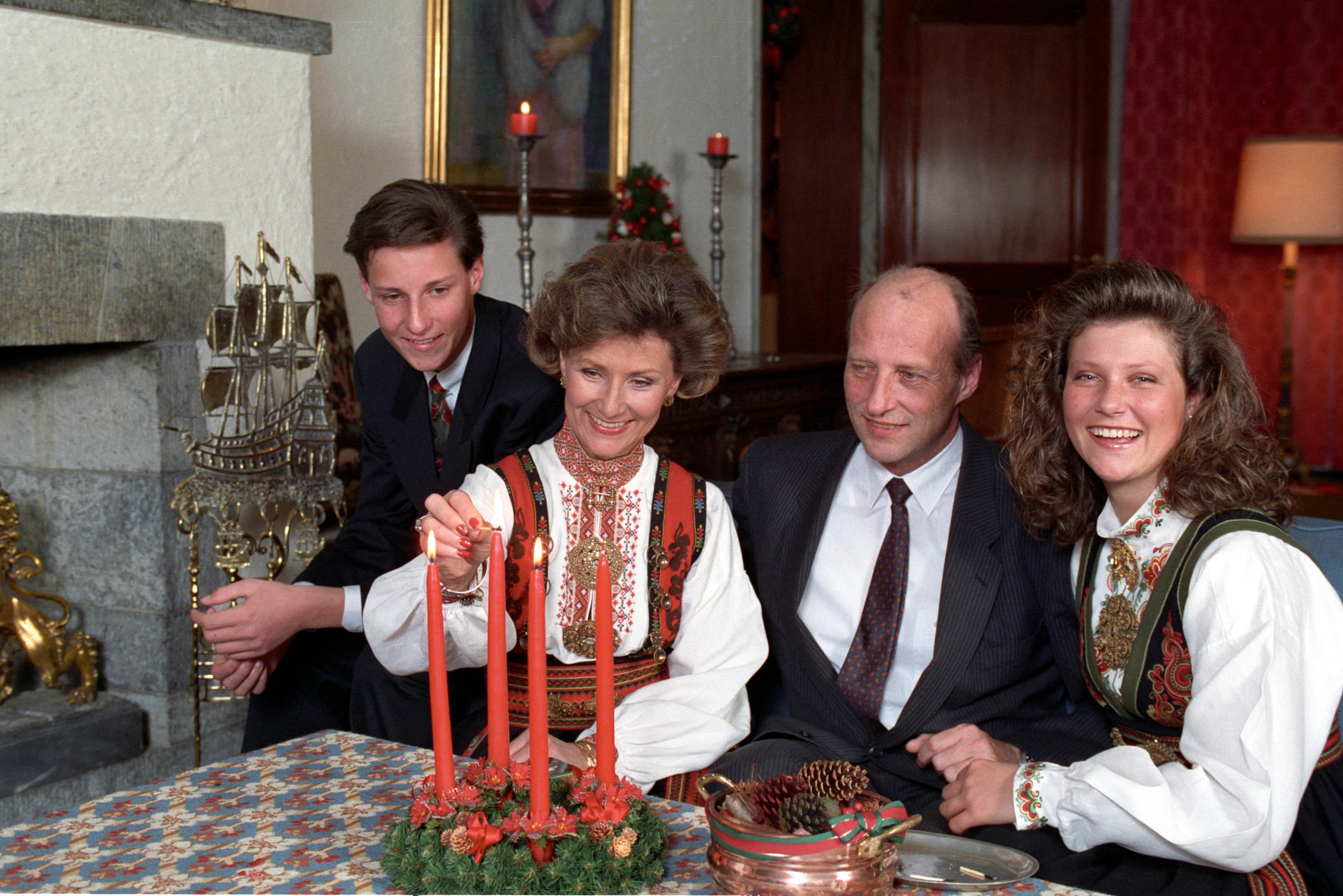 Kronprinsesse Sonja tenner adventslysene med barna og ektemannen rundt seg. Kvinnene i bunad, og mennene i dress.