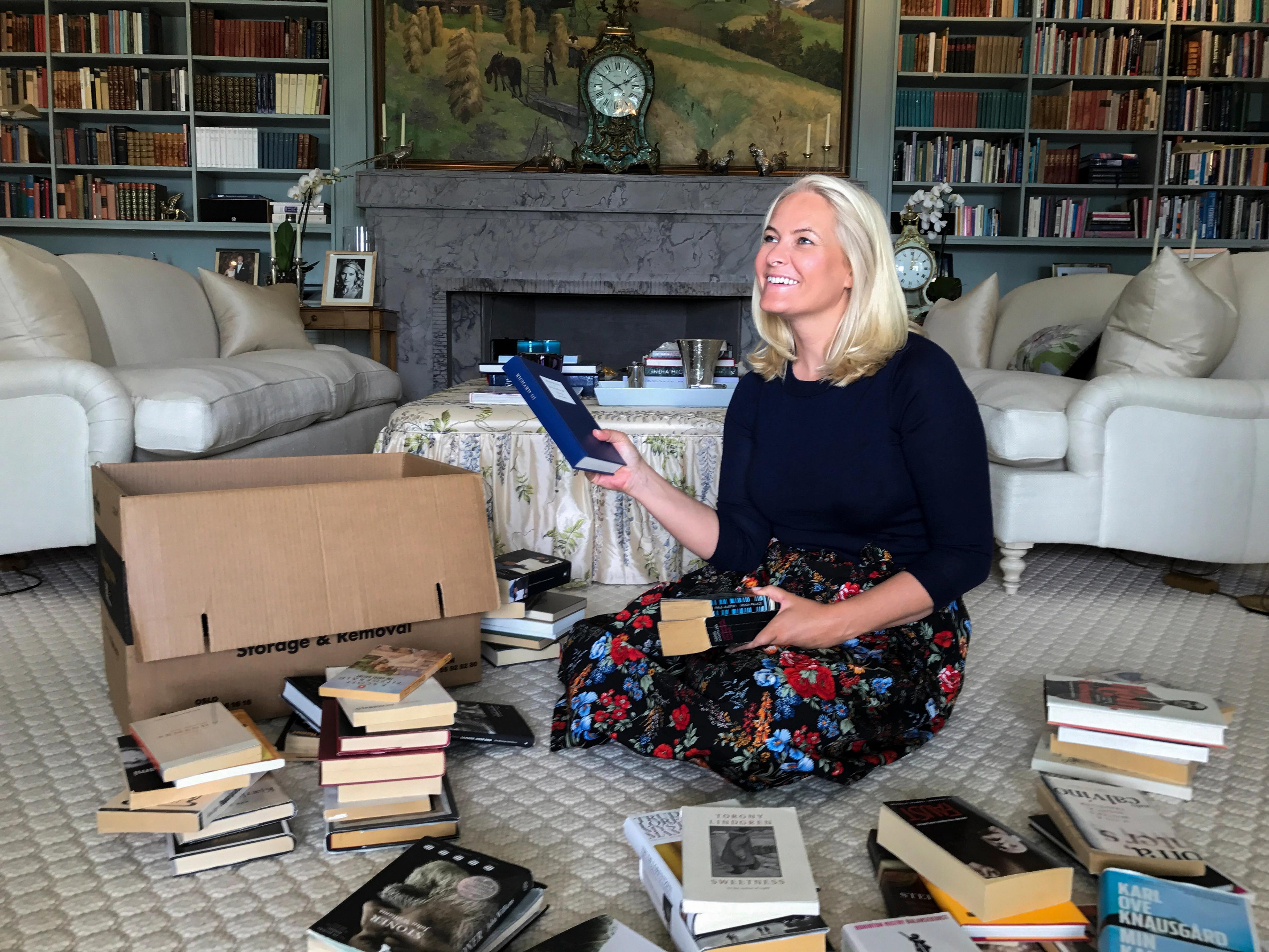 Kronprinsessen sitter smilende på gulvet, omkranset av bøker.