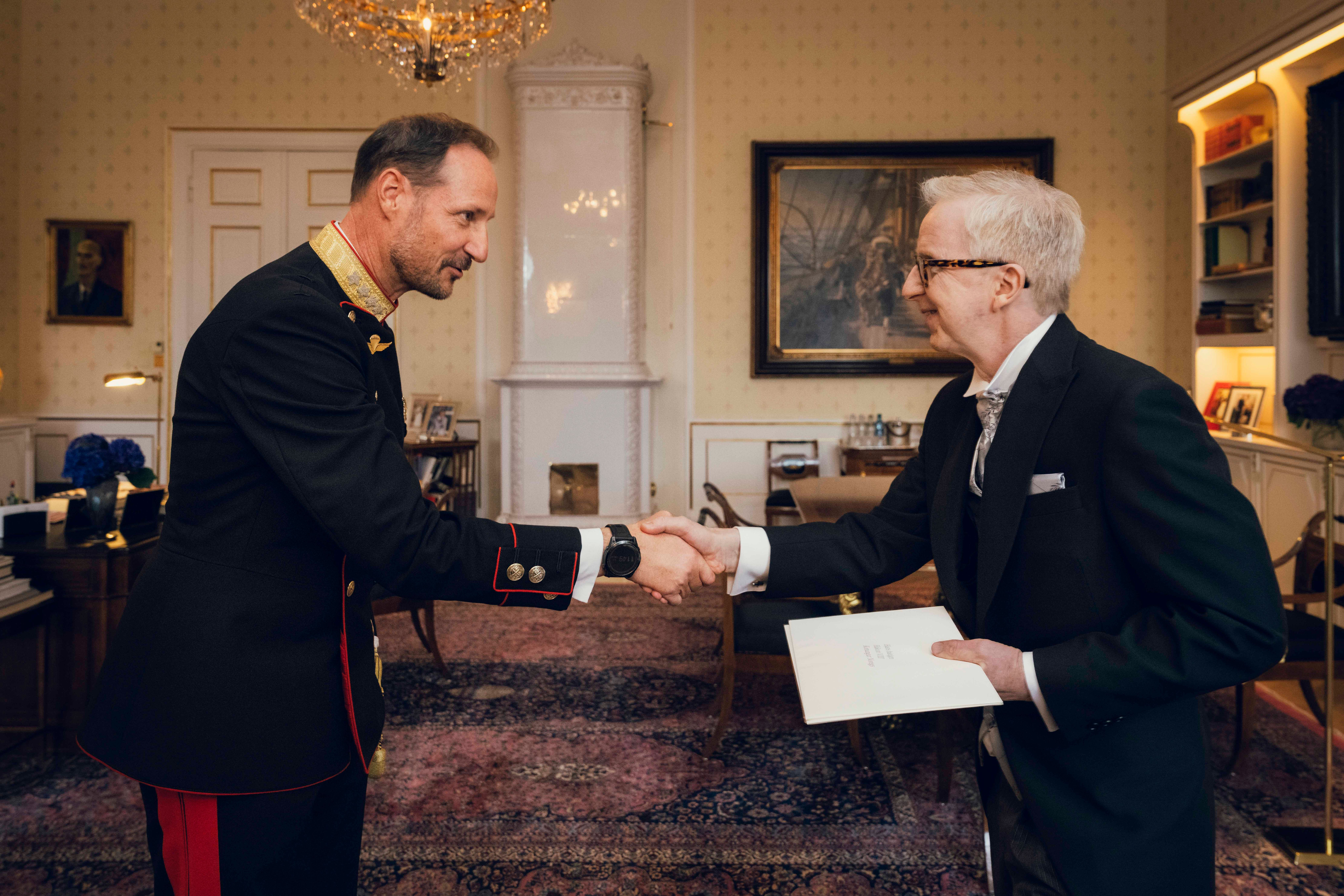 Kongen og ambassadøren håndhilser på Kongens kontor. Ambassadøren holder en stor konvolutt med sine akkreditiver i hånden.