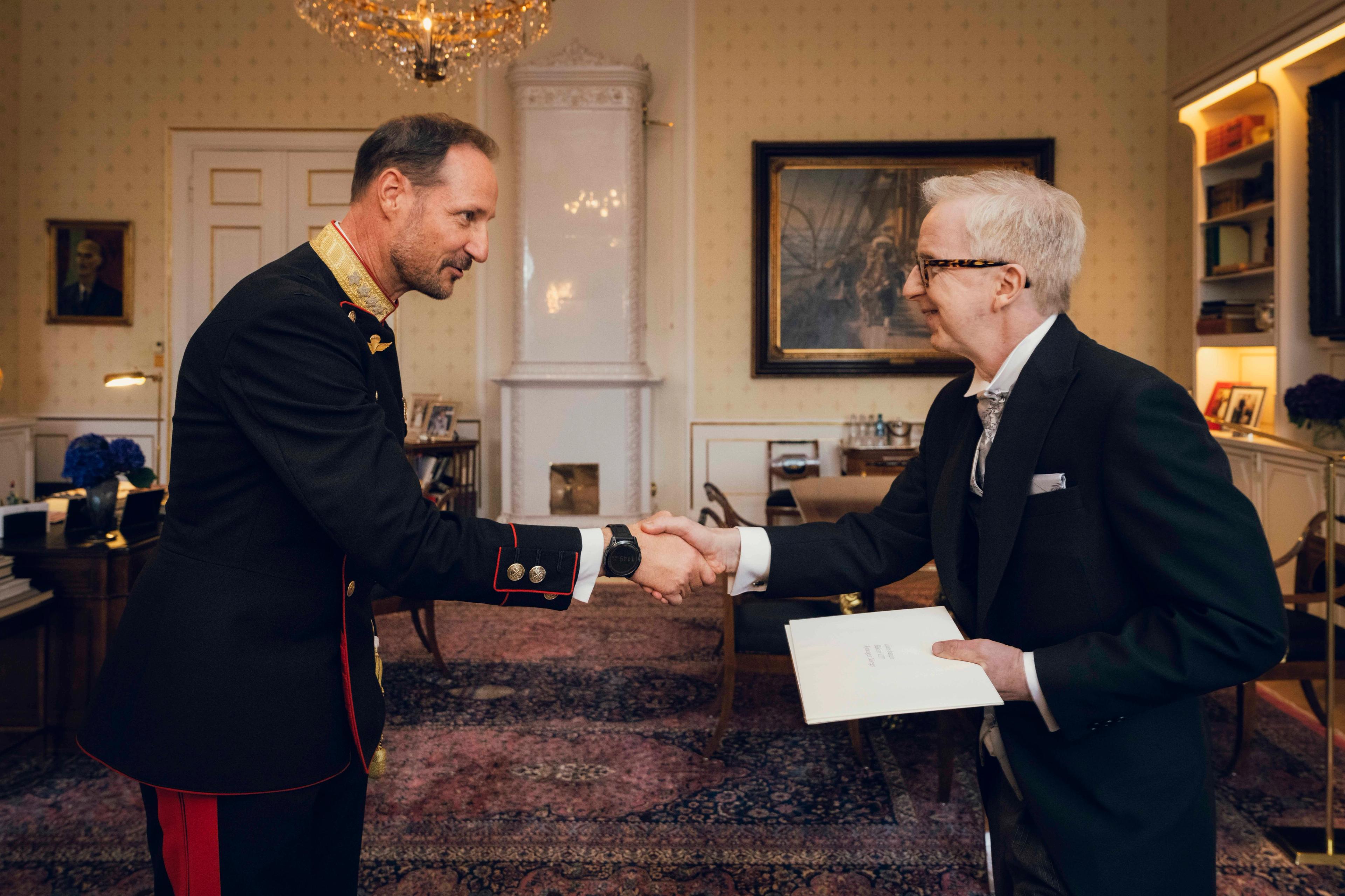 Kongen og ambassadøren håndhilser på Kongens kontor. Ambassadøren holder en stor konvolutt med sine akkreditiver i hånden.