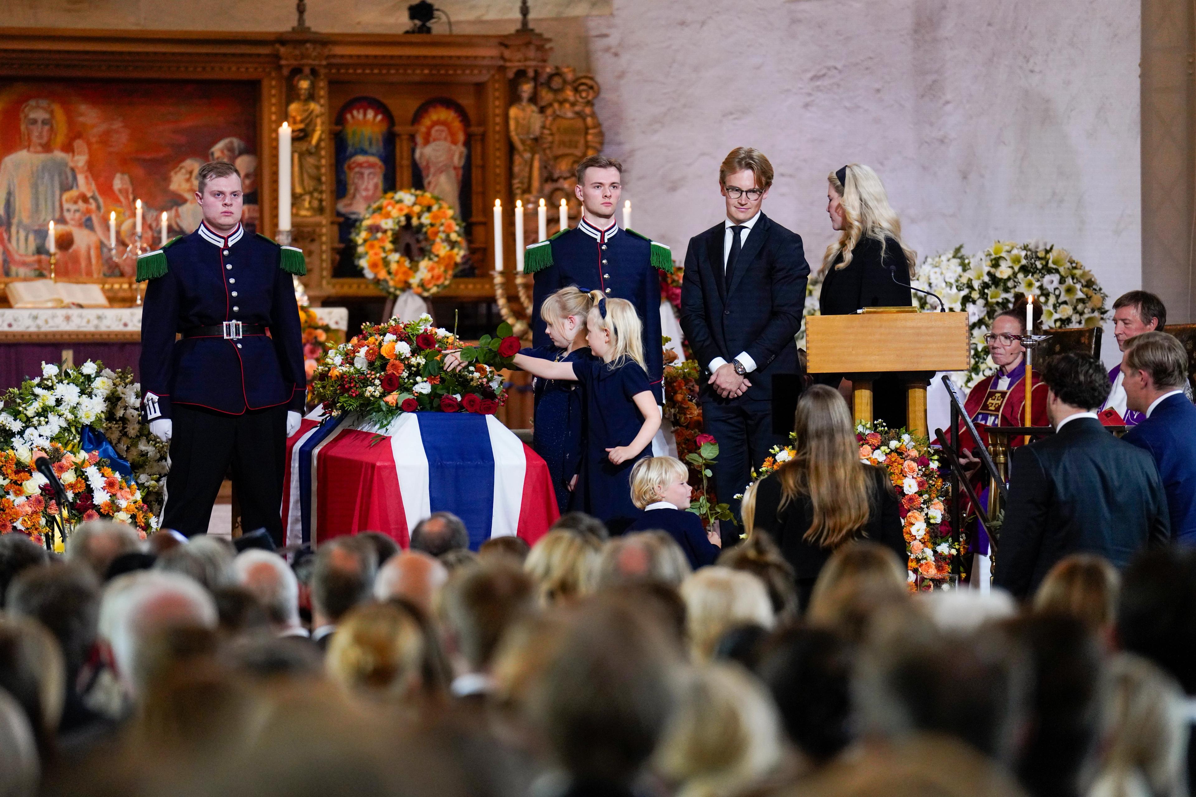 To små lyshårede jenter legger hver sin rose på båren, som er hyllet inn i det norske flagget.