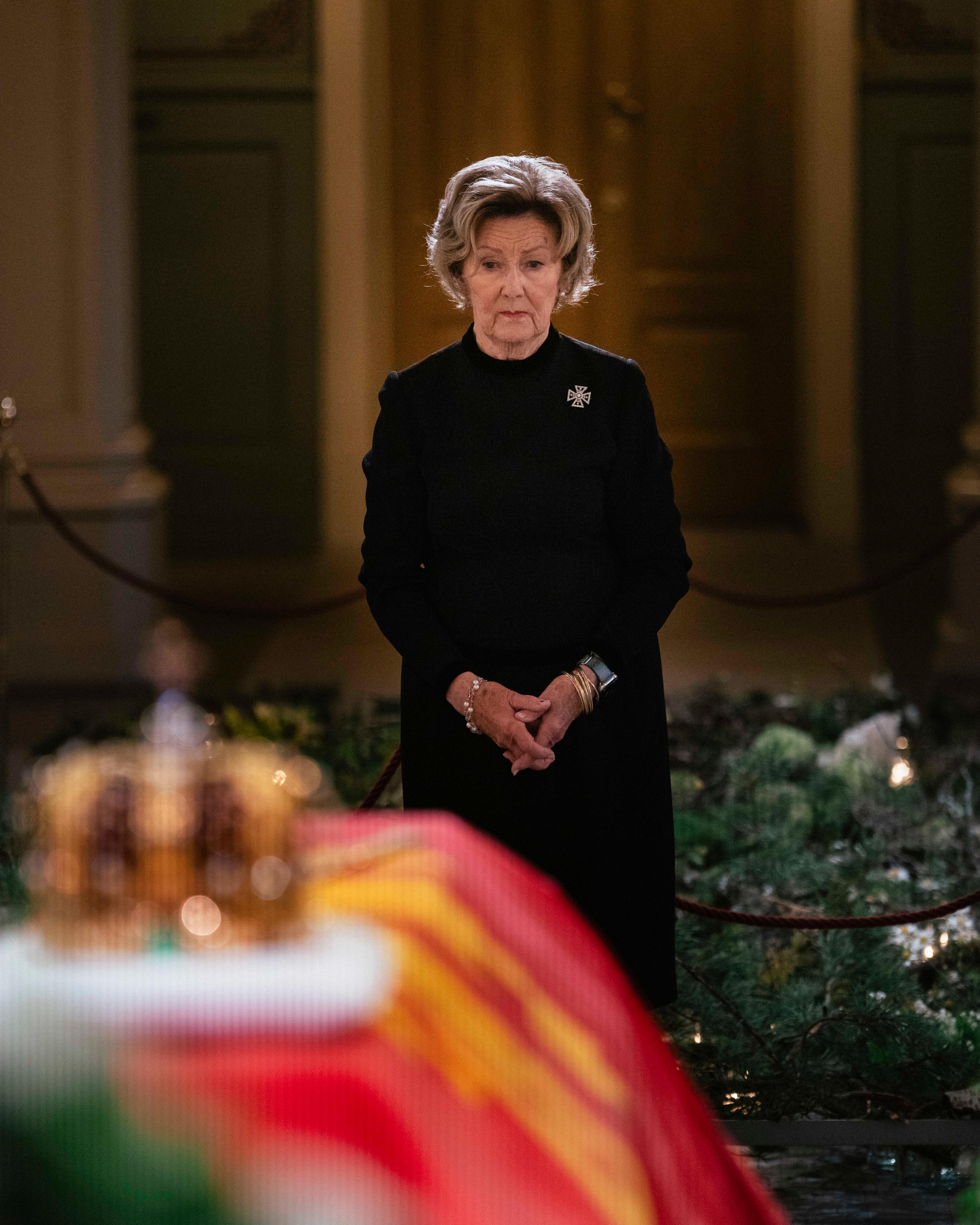Dronning Sonja i sort står foran Kong Haralds båre.