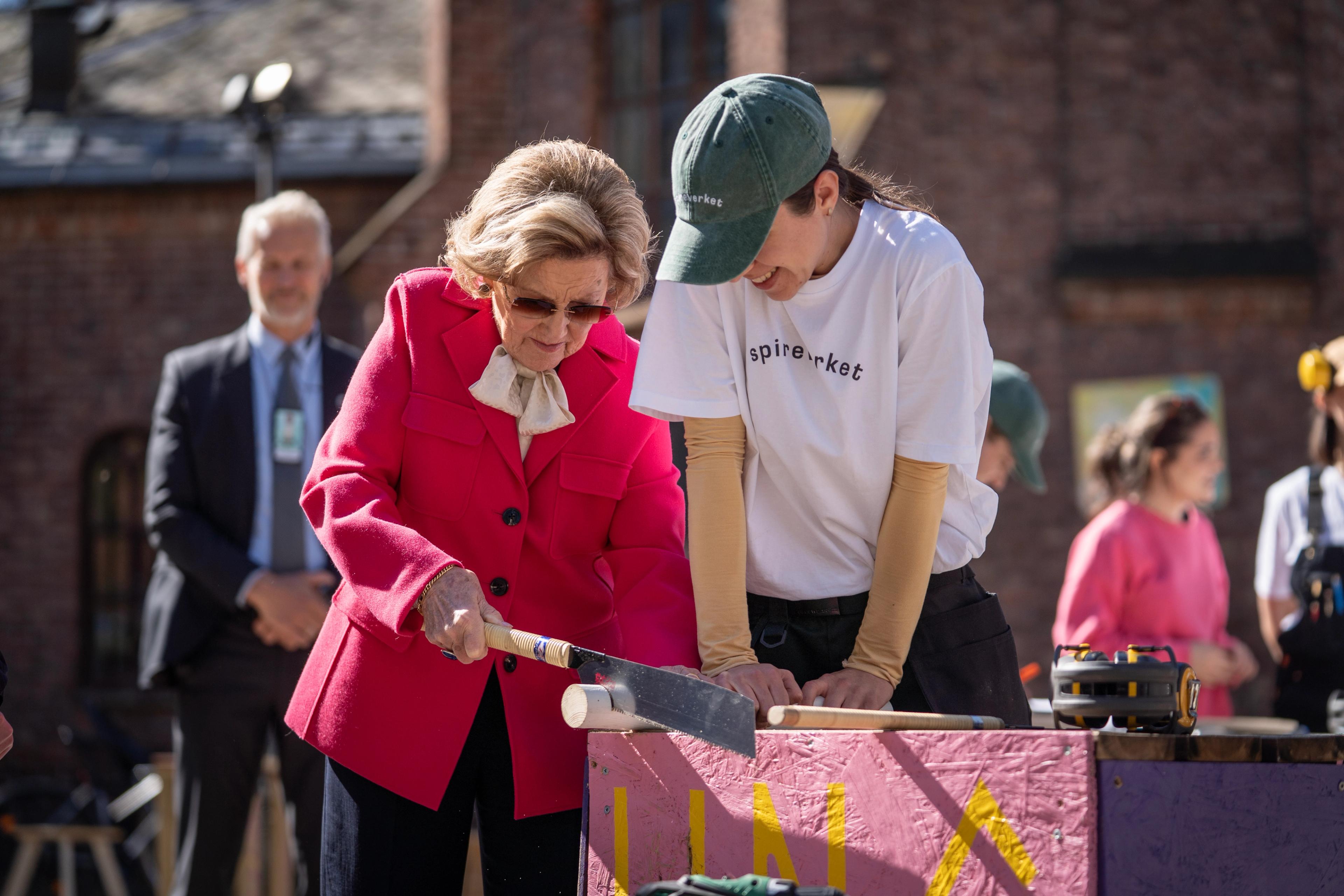 Dronning Sonja sager et bordbein, mens en ansatt i Spireverket bistår med å holde trebeinet fast.