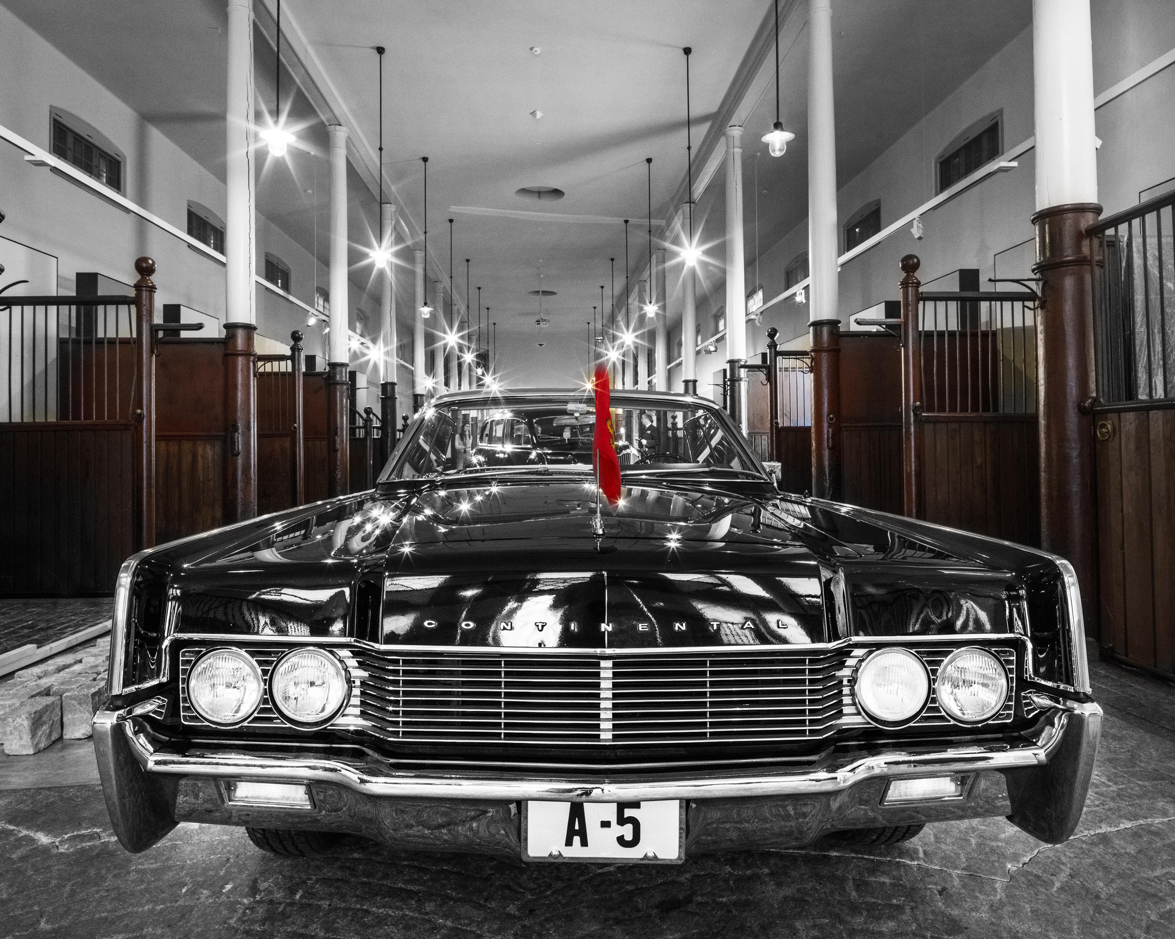 Nærbilde av en sort veteranbil, sett forfra, med detaljer i krom og Kongefalgget i front. Bakover i bildet synes spiltauene i KunstStallen. Foto: Øivind Möller Bakken, Det kongelige hoff