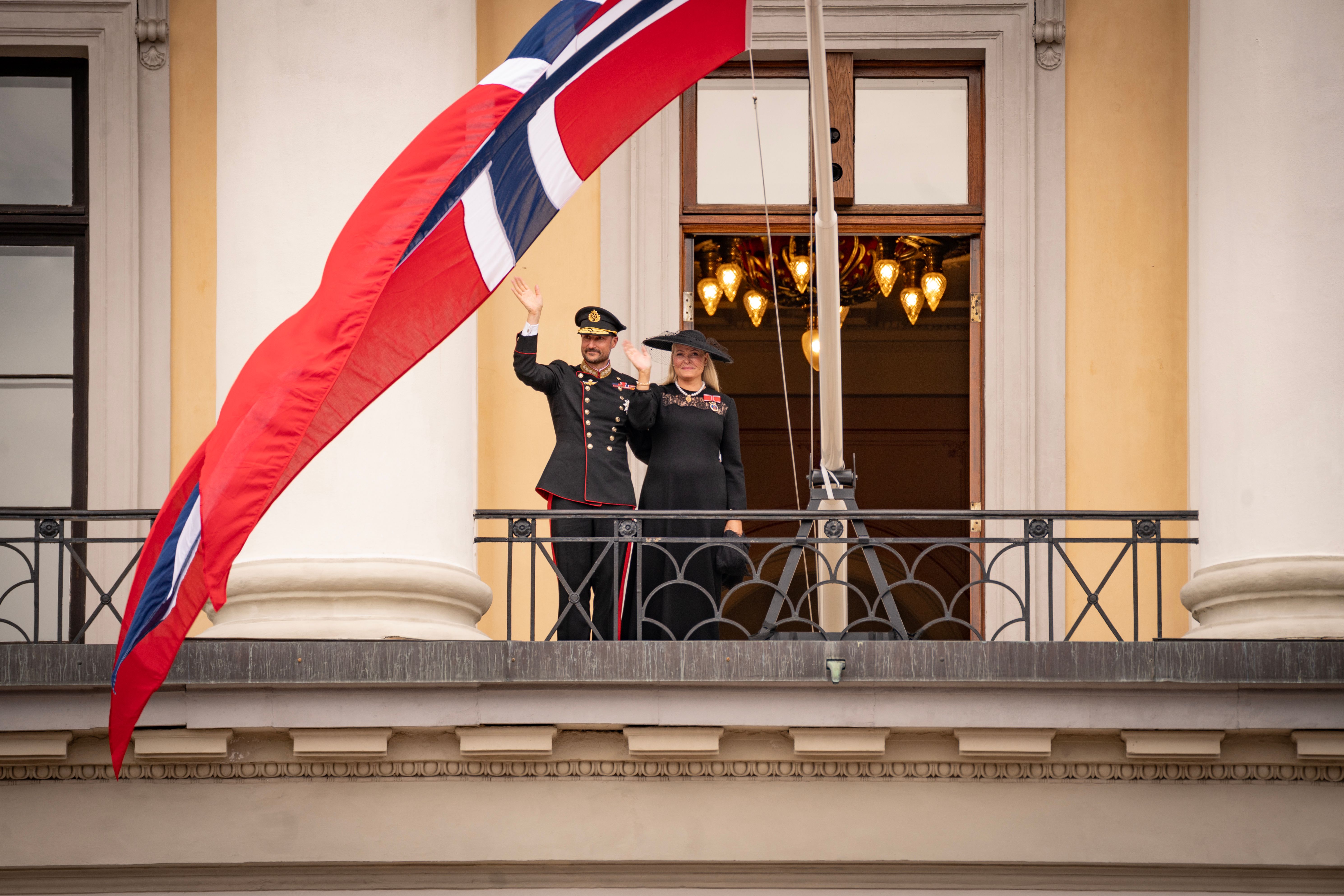 Kongeparet i sorte klær - Kongen i uniform - vinker fra Slottsbalkongen.