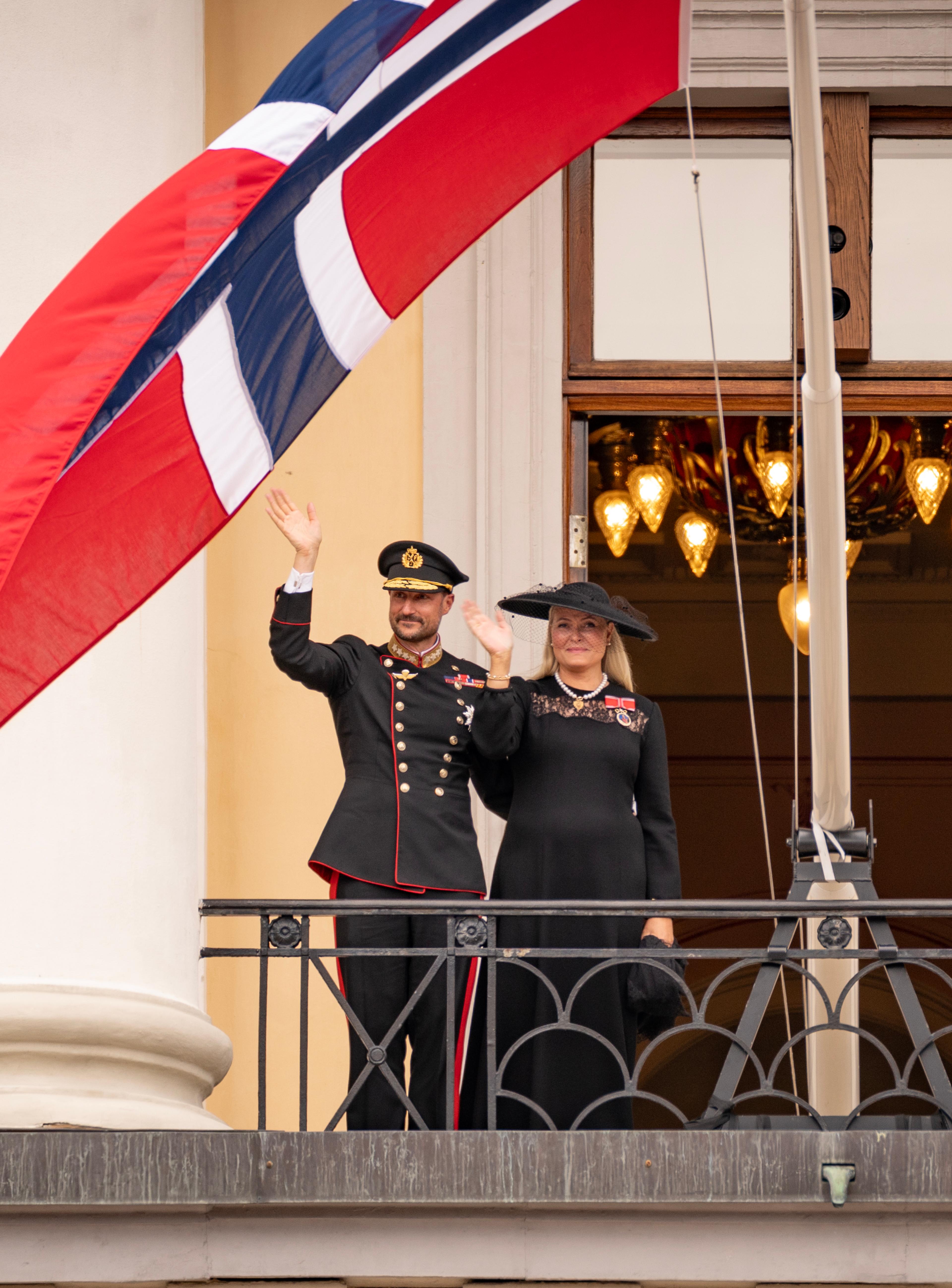 Kongeparet i sorte klær - Kongen i uniform - vinker fra Slottsbalkongen.