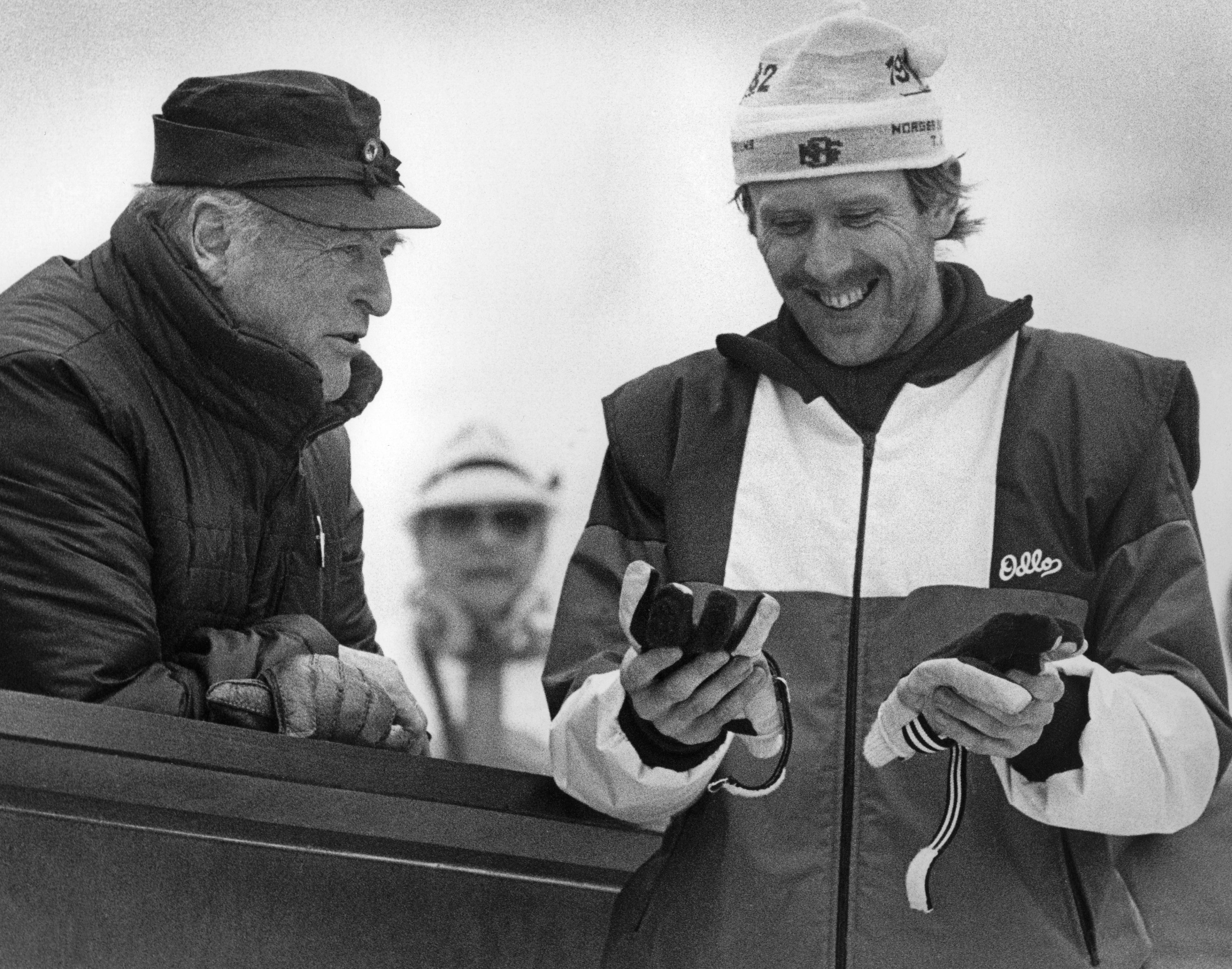 Kongen lener seg over tribunen der han står og snakker med en smilende Oddvar Brå.