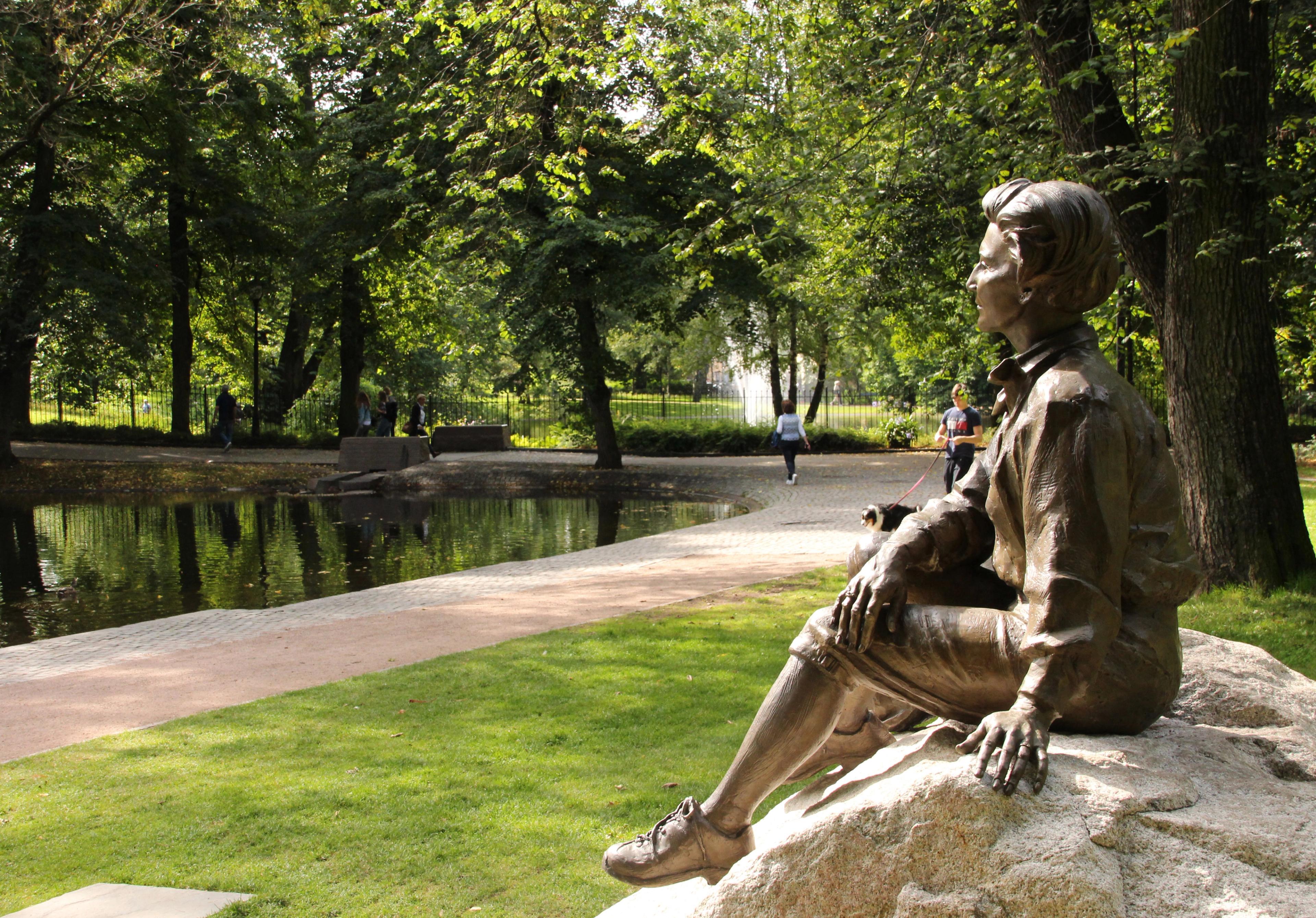 Dronningen, støpt i bronse, sitter med tursekken sin på en stein og ser utover parken.