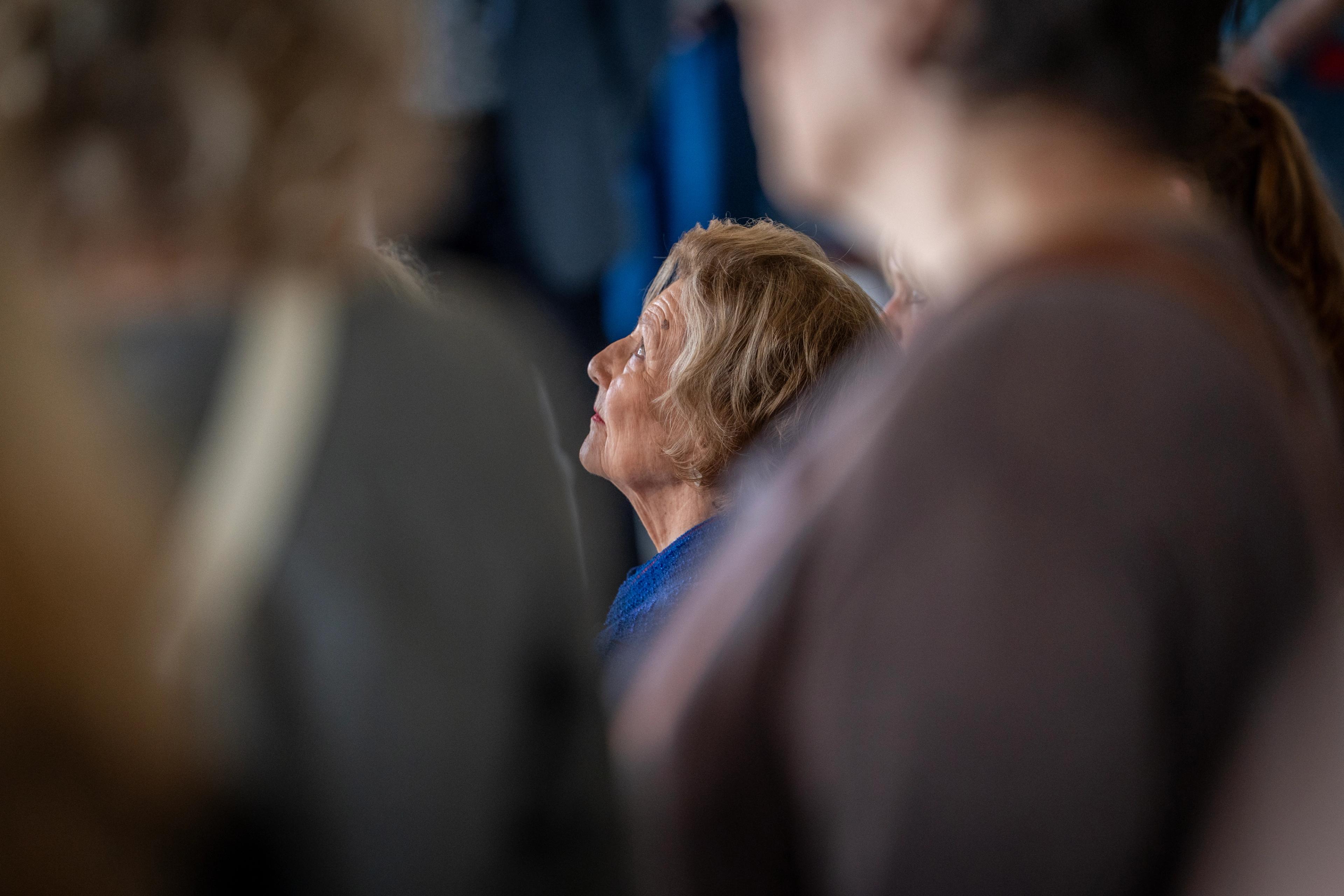 Dronning Sonja skimtes mellom mennesker vi ikke ser ansiktet på. Hun ser oppover.