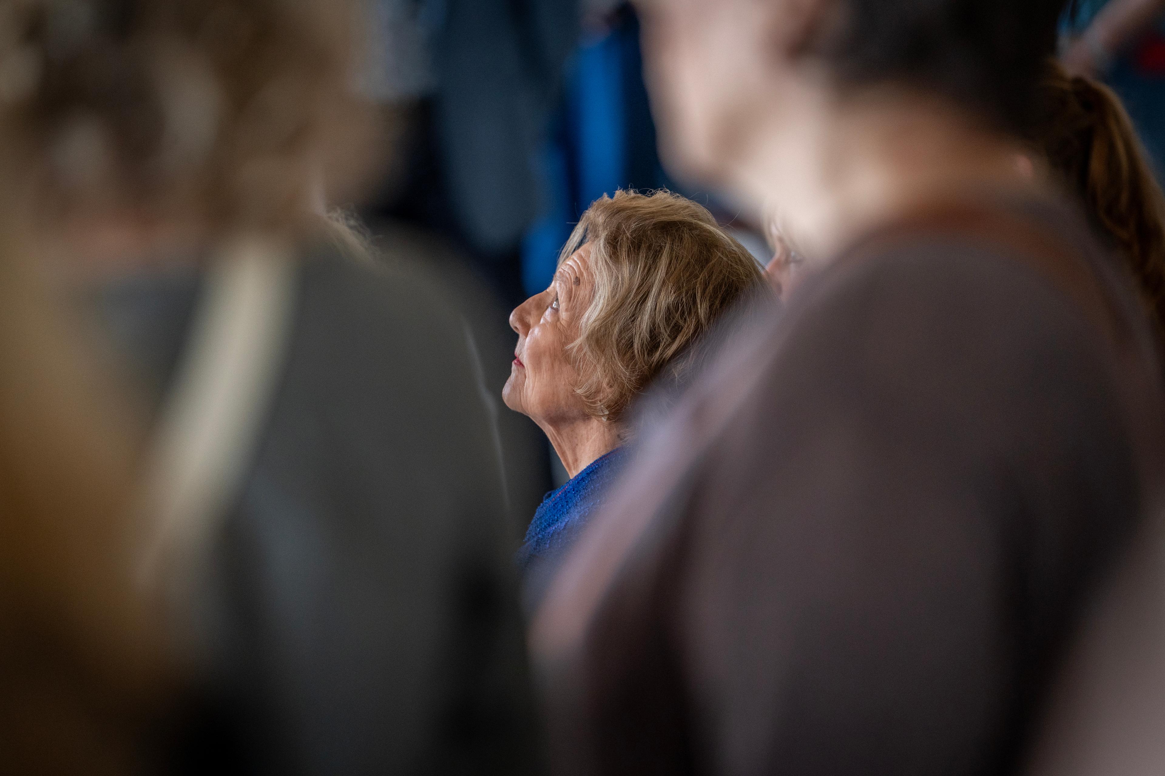 Dronning Sonja skimtes mellom mennesker vi ikke ser ansiktet på. Hun ser oppover.