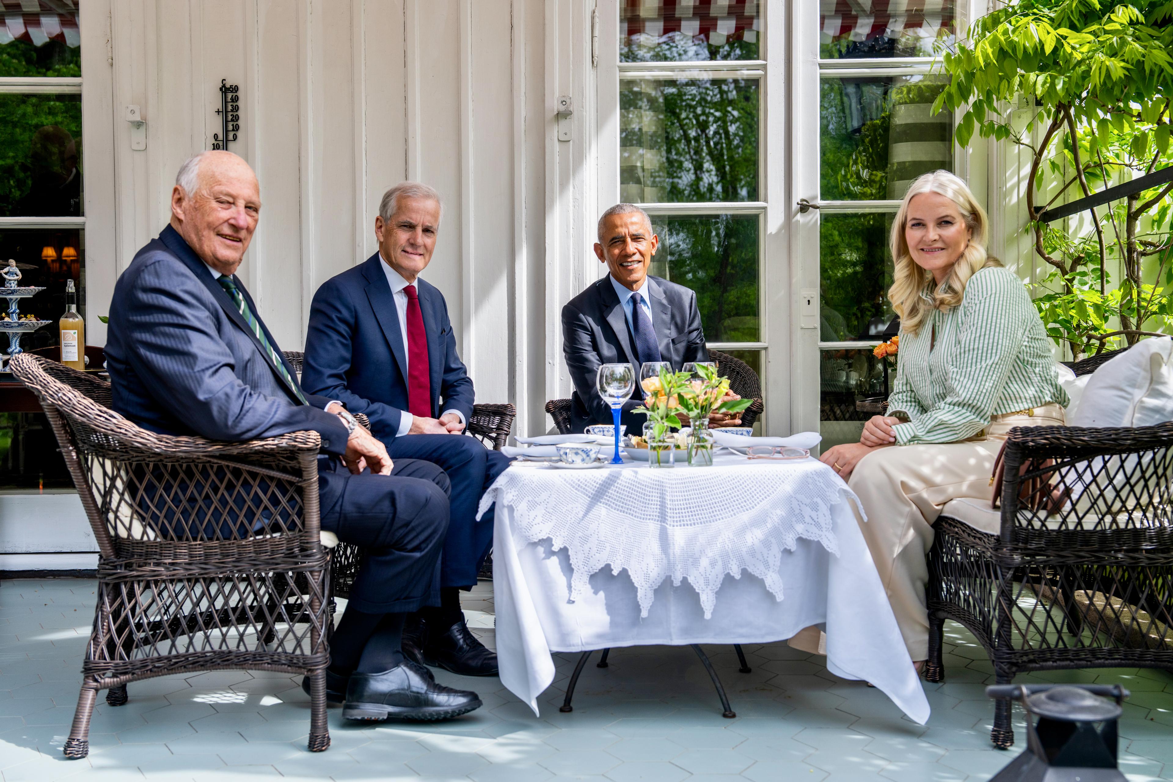 Kong Harald, statsminister Jonas Gahr Støre, USAs tidligere president Barack Obama og Kronprinsesse Mette-Marit sitter rundt et bord på en terrasse.