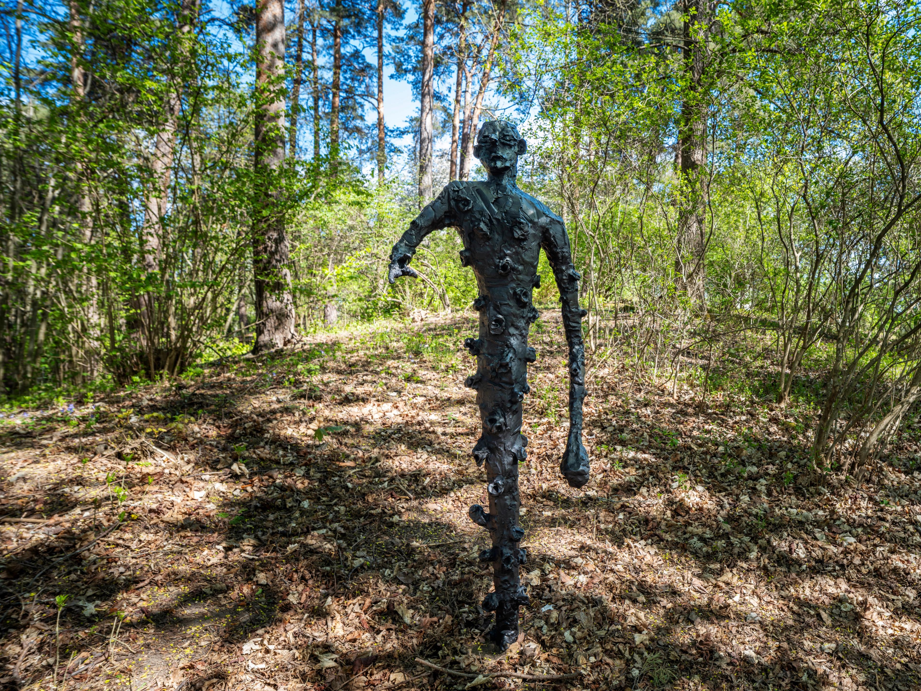 Bronseskulptur av en skikkelse med en kort og en lang arm, ser ut til å være på vei gjennom skogen.