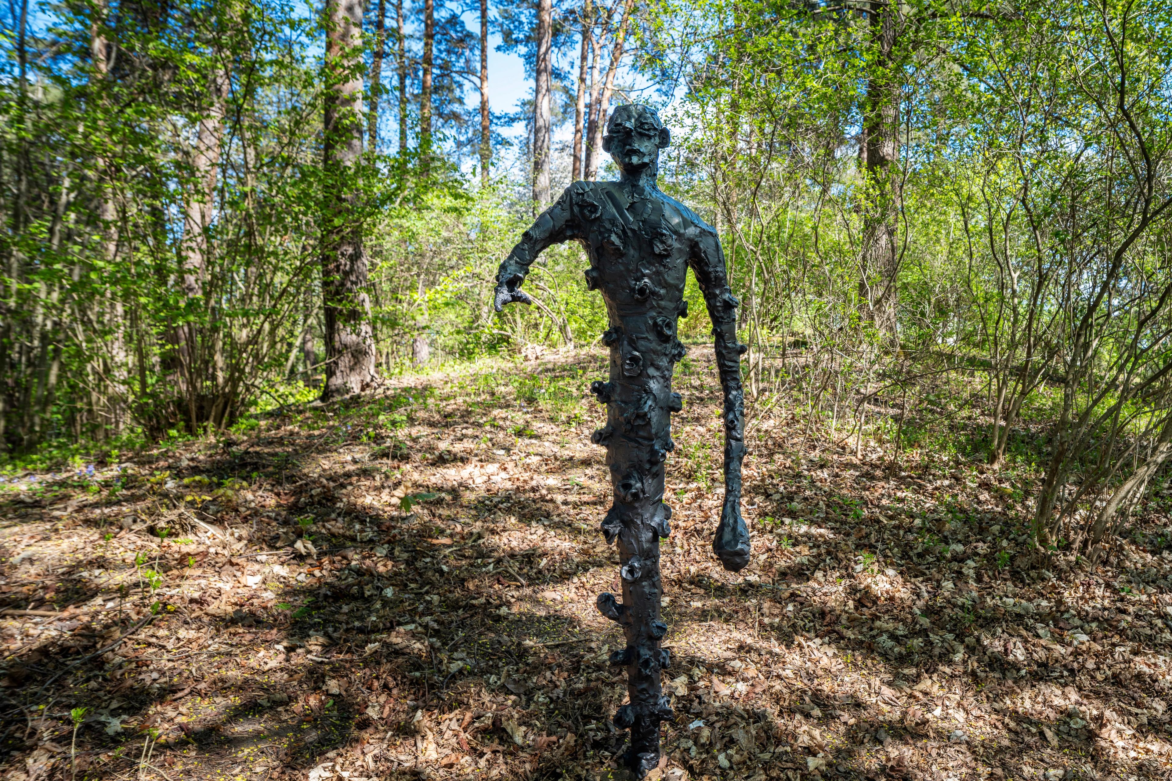 Bronseskulptur av en skikkelse med en kort og en lang arm, ser ut til å være på vei gjennom skogen.