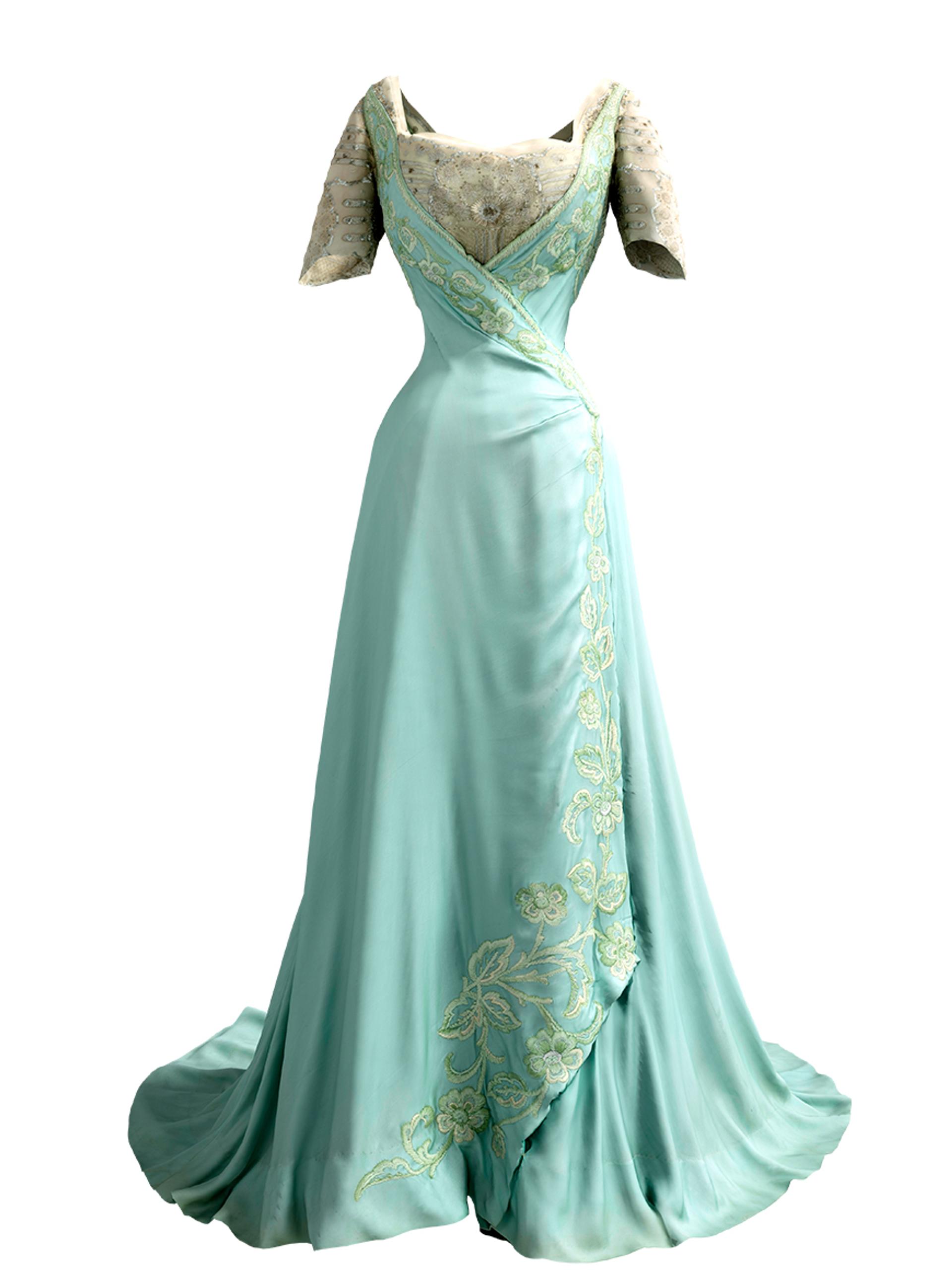 En turkis, fotsid kjole med blomsterbroderier i hvitt og gull og svøpt liv.