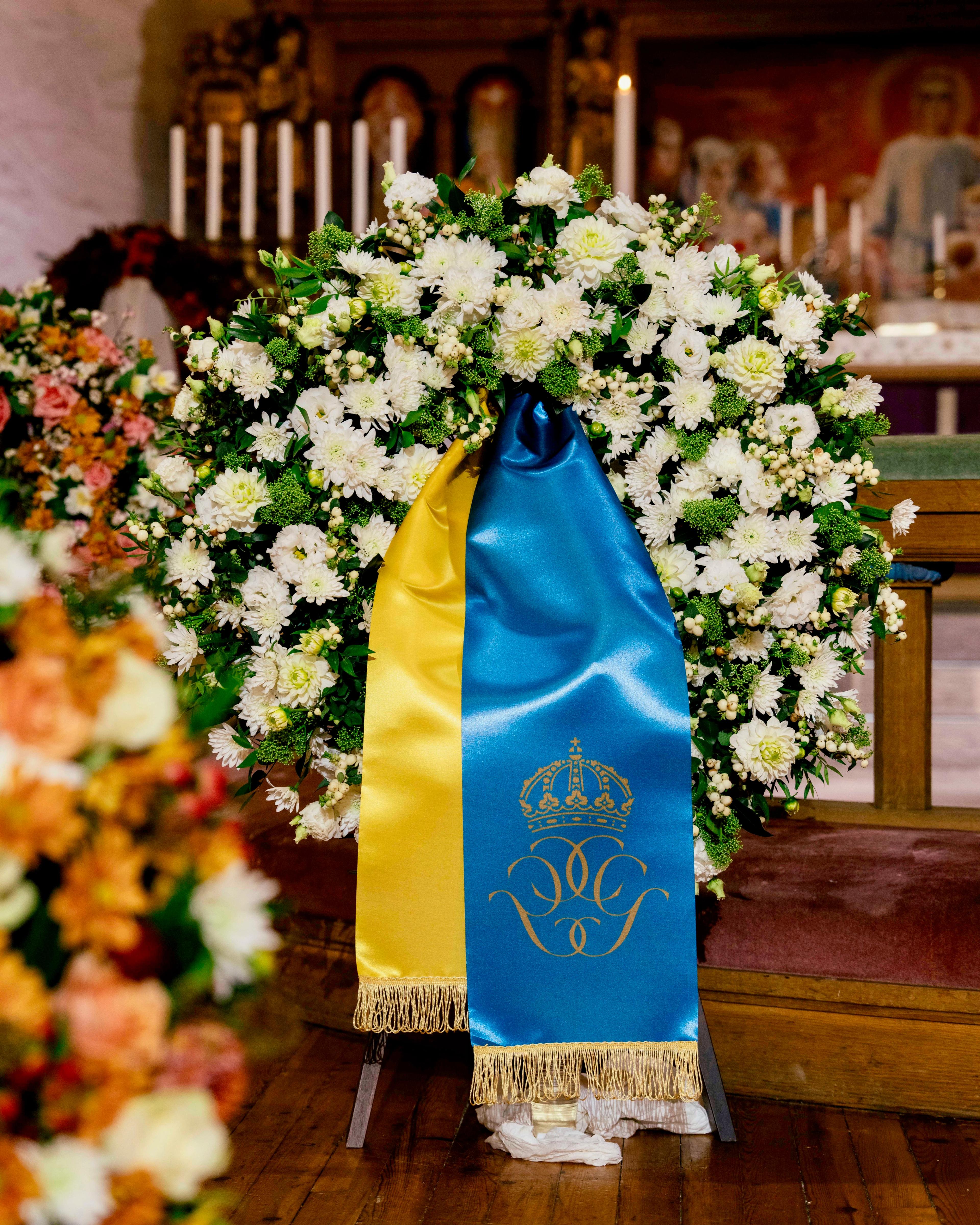 Blomsterkrans med bånd i fargene til det svenske flagget og monogrammet til Kong Carl XVI Gustaf og Dronning Silvia av Sverige.