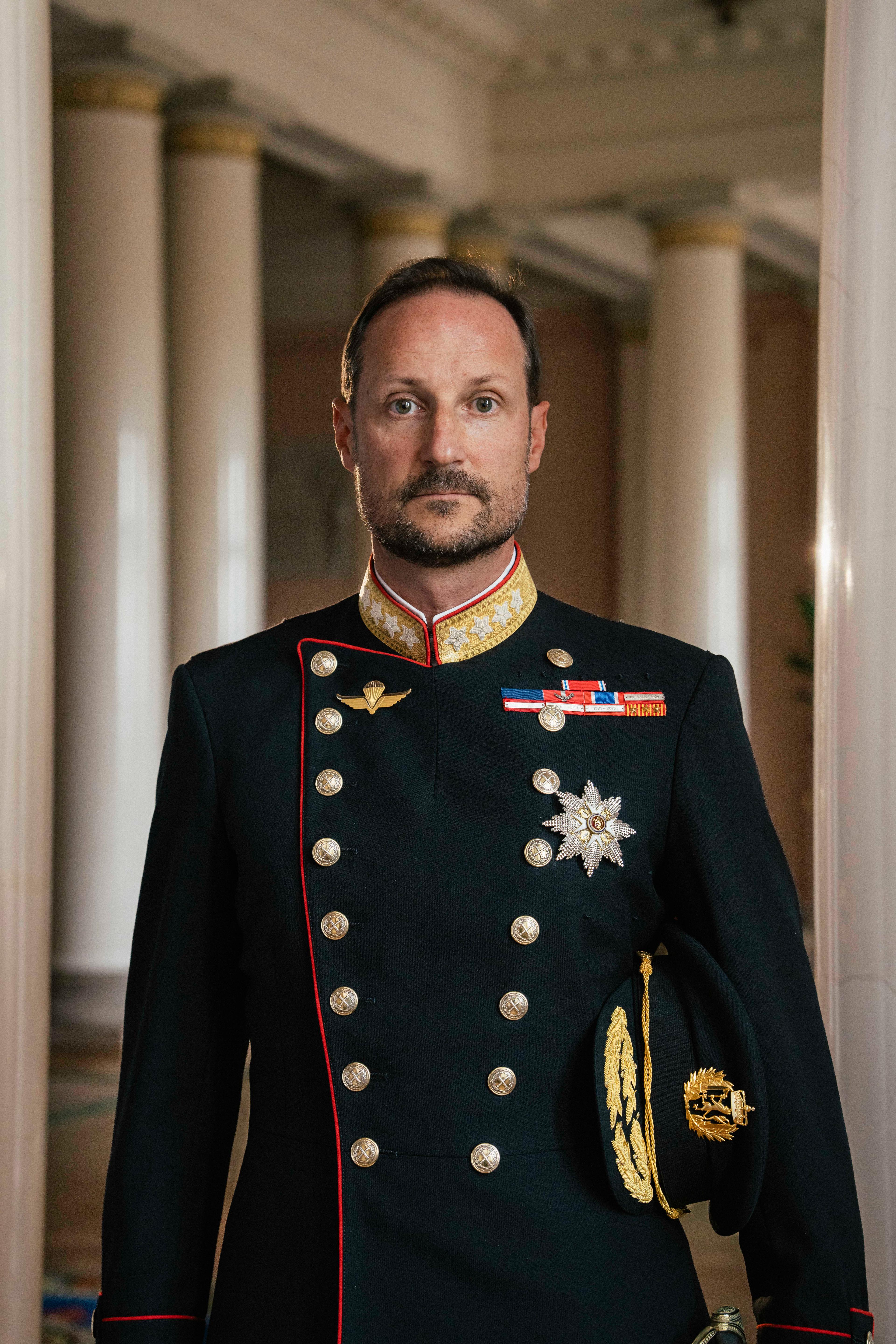 Kong Haakon stående i gallauniform med ordener og medaljer.