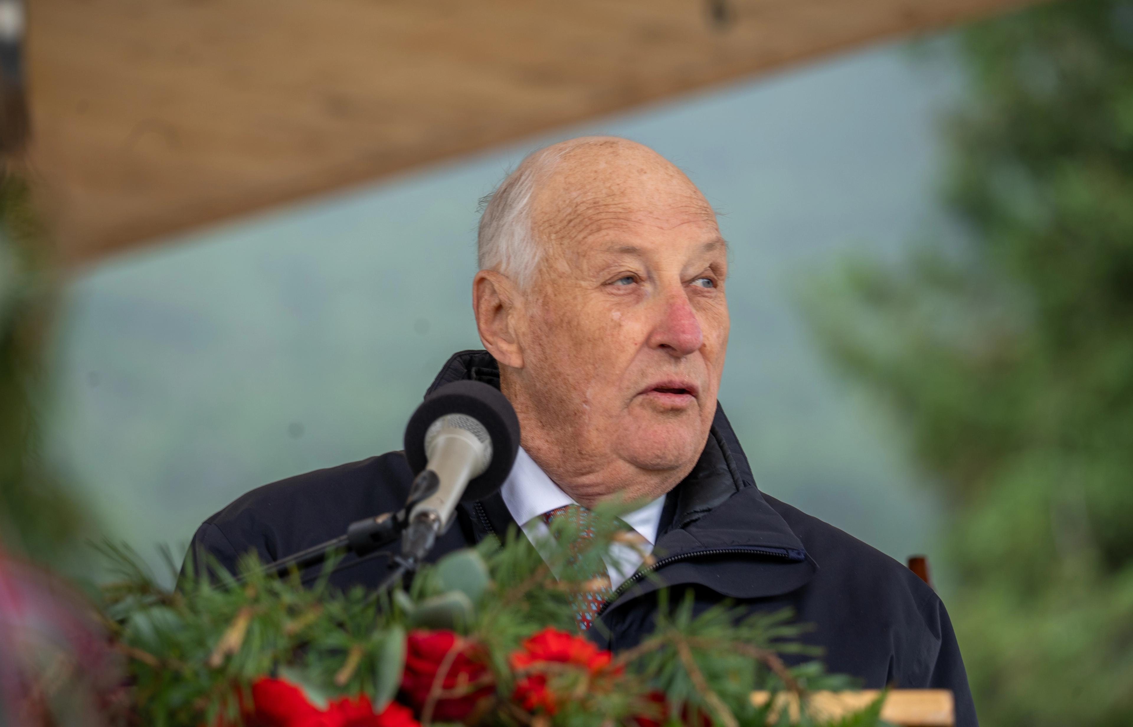 Kongen står ved talerstolen, foran en mikrofon. Han har blå jakke og talekort i hendene.,