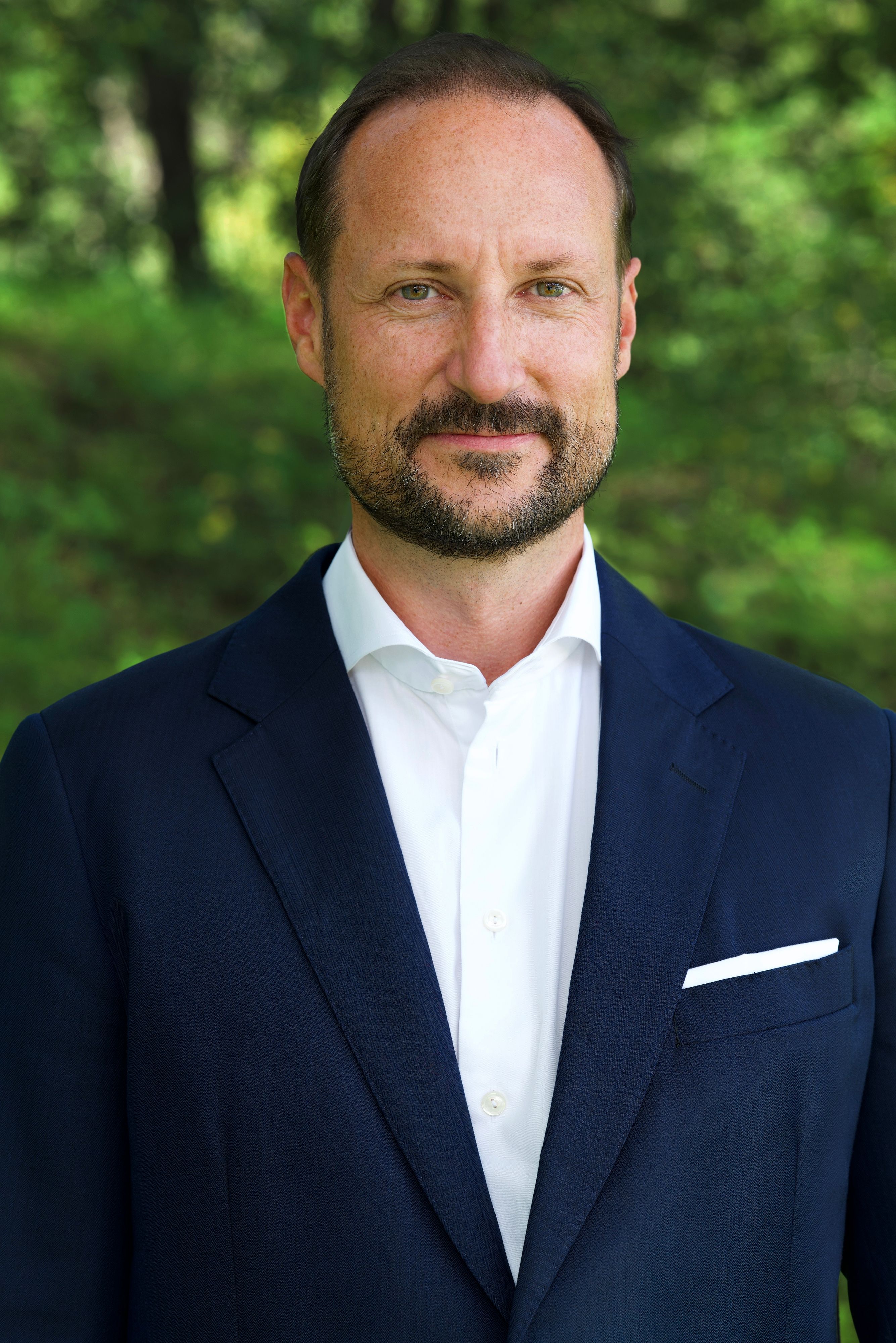 Portrett av Kronprins Haakon tatt ute i hvit skjorte uten slips og blå dress.