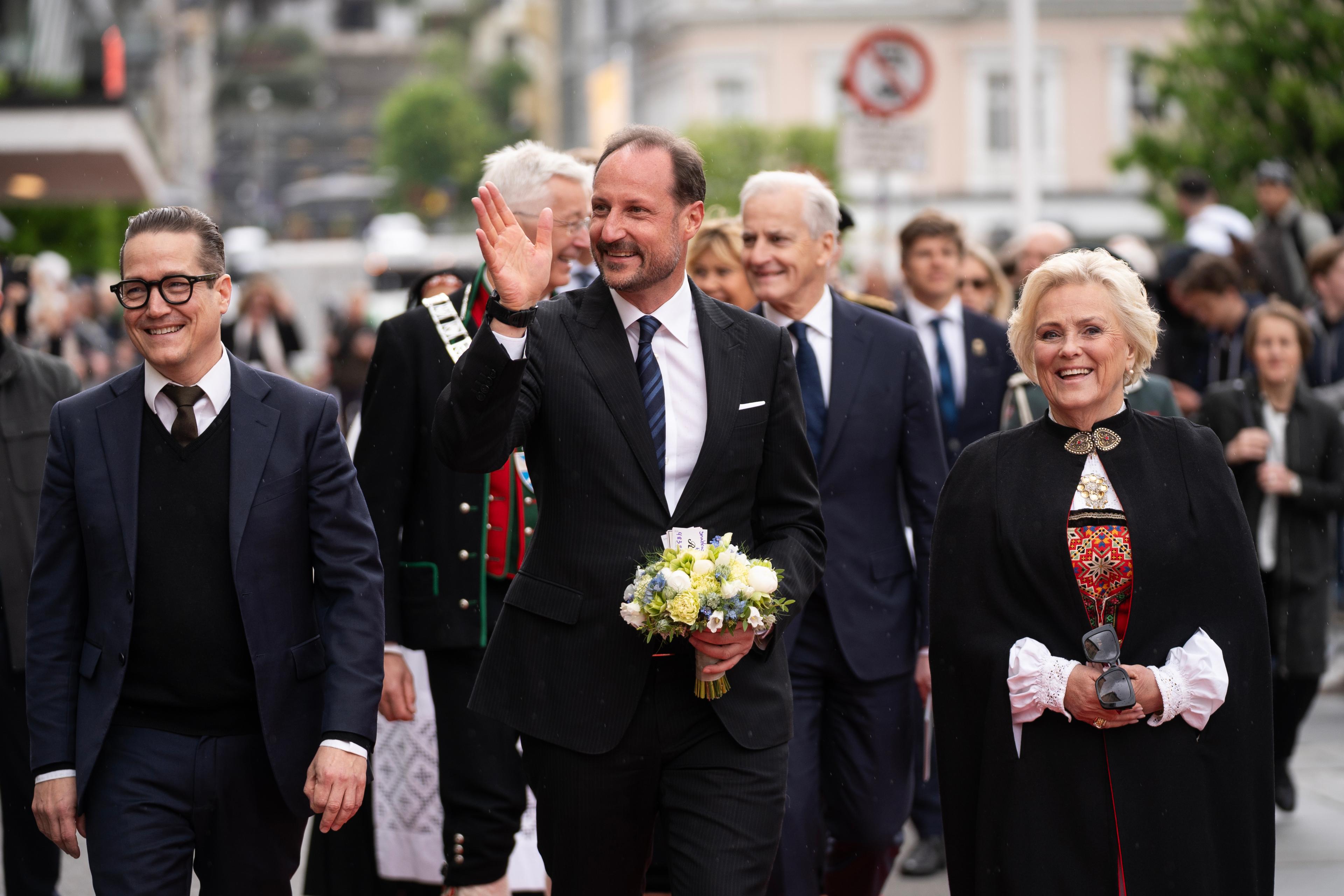 Kronprinsen kommer gående langs rød løper med blomster i hendene og mennesker rundt seg.