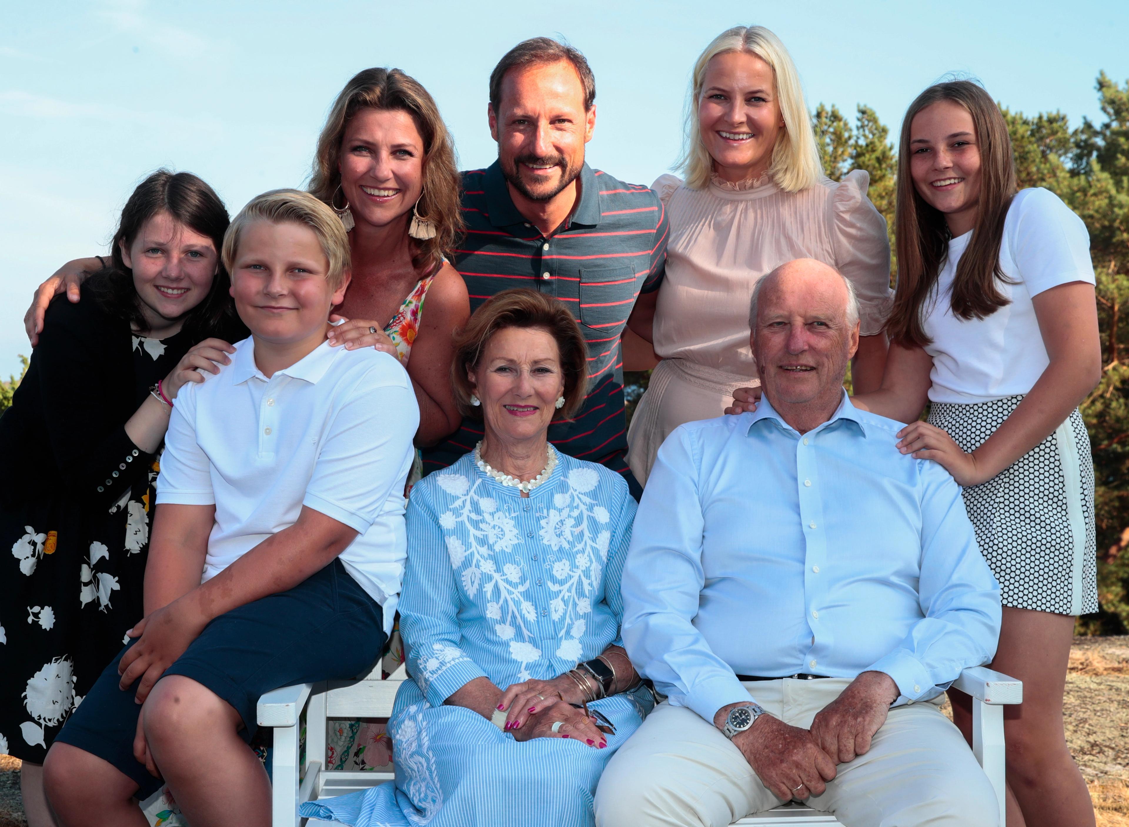 Kong Harald og Dronning Sonja sitter på en hvit benk med barn, svigerdatter og barnebarn rundt seg.