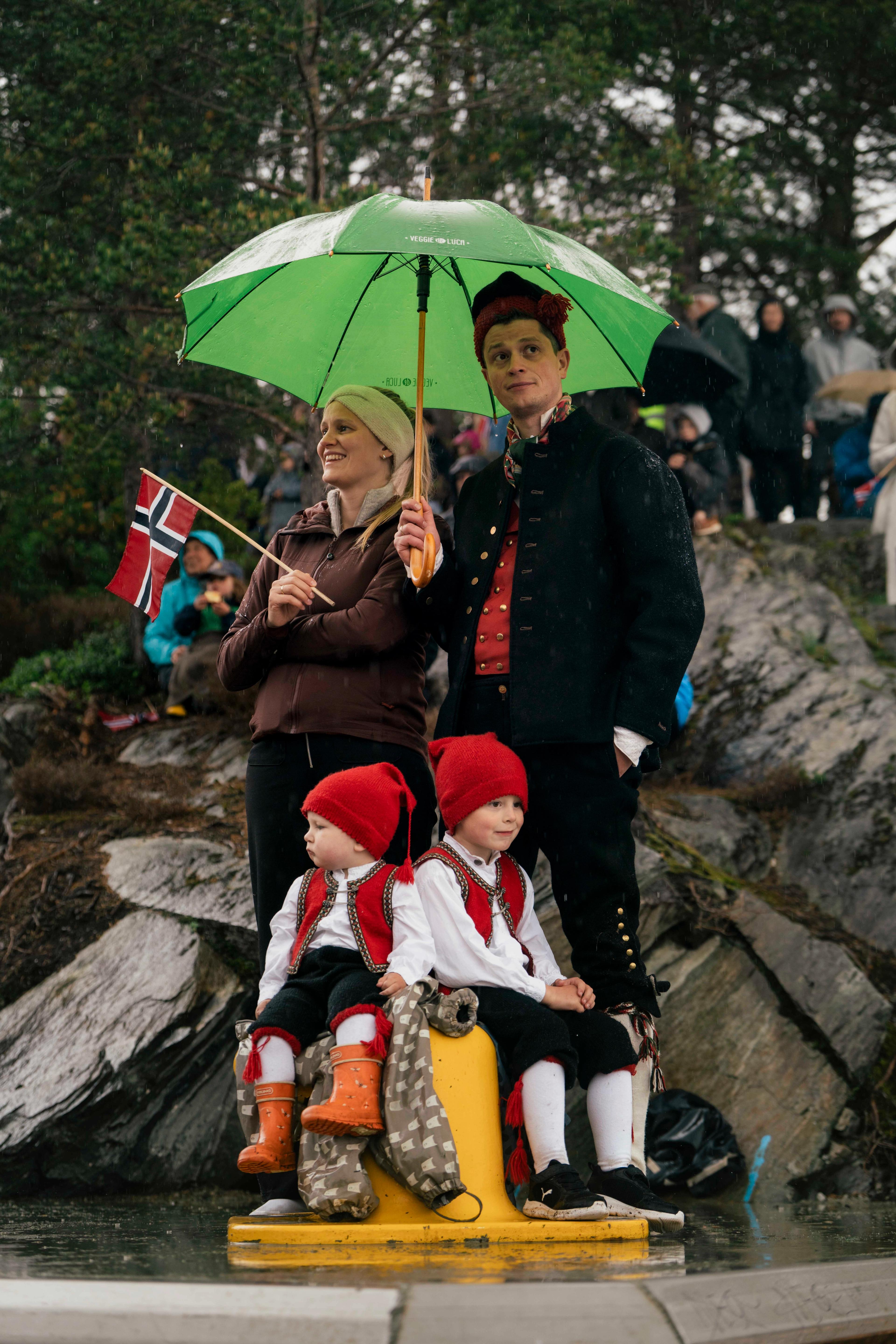 Ein familie på fire ikledd bunad og undere ein stor, grøn paraply.