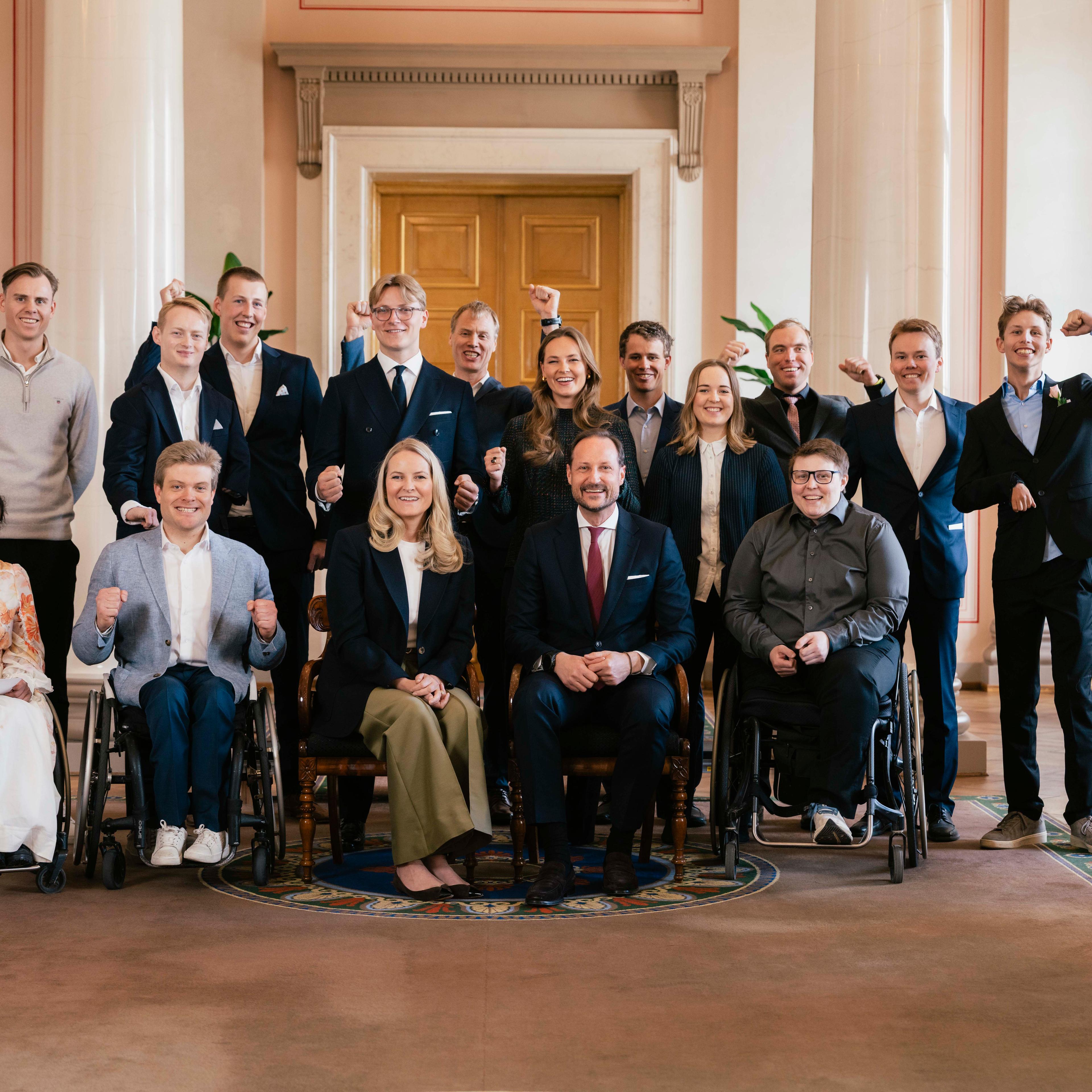 Kronprinsparet, Prinsesse Ingrid Alexandra og Prins Sverre Magnus omgitt av de norske deltakerne i Paralympics 2026. Kronprinsparet sitter på første rad sammen med utøvere i rullestol, mens Prinsessen og Prinsen står på andre rad sammen med de andre utøverne.
